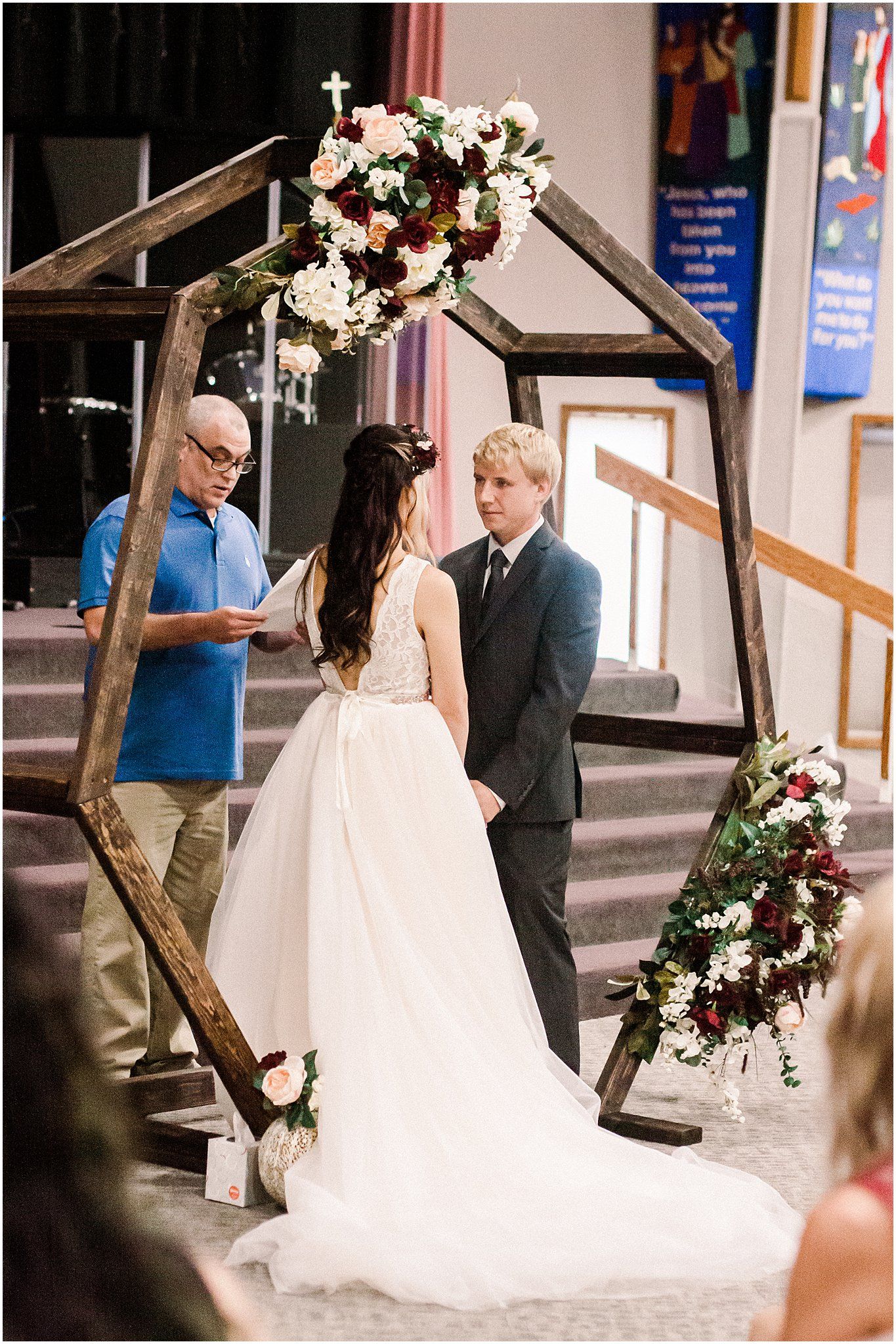 Wedding ceremony under wooden arch decorated with white and burgundy flowers.