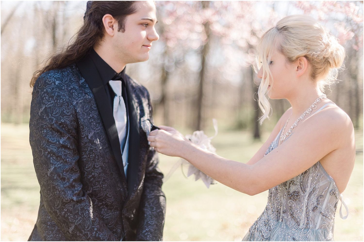 Two people in formal attire adjust clothing details during an outdoor photoshoot.