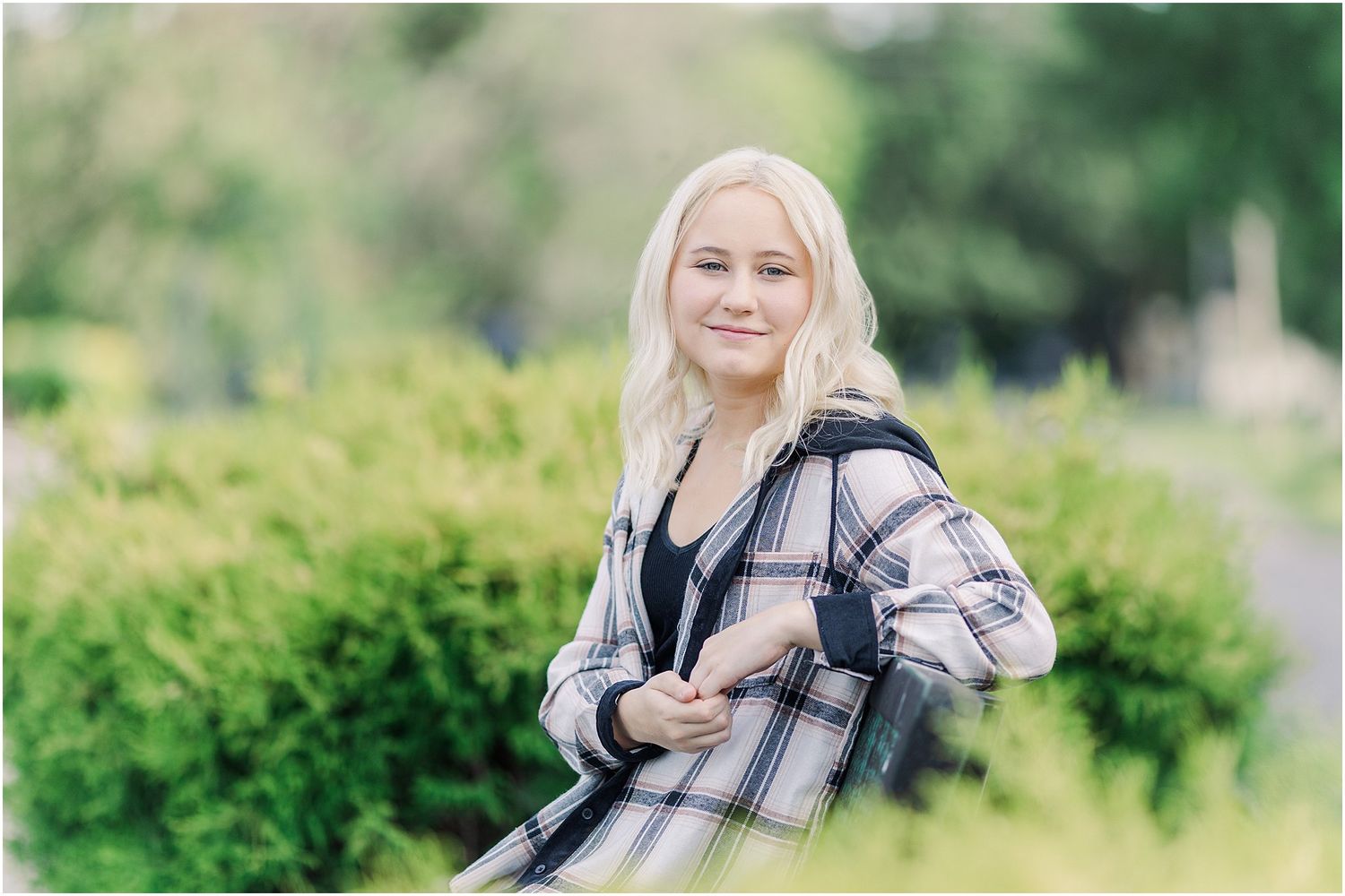 Senior girl sitting on bench in between two boxwood shrubs