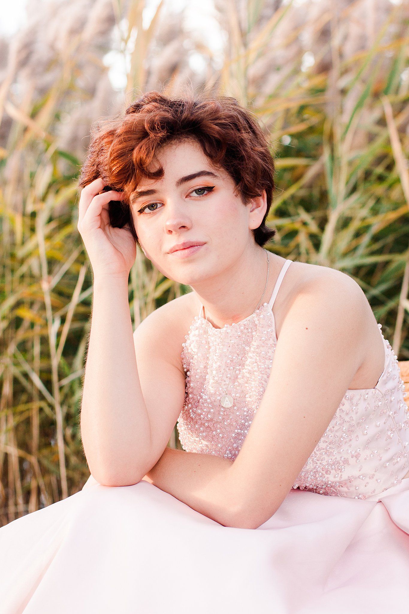 Dreamy portrait in pink sequined dress amid tall grass at golden hour.