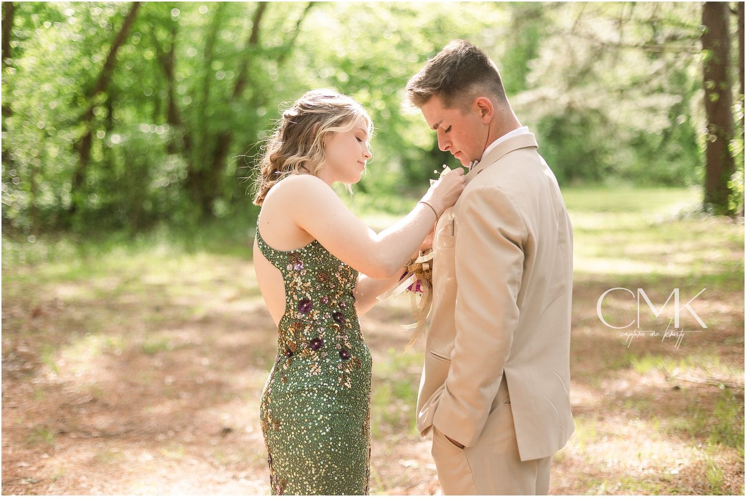 A tender moment captured as a couple adjusts their formal wear in a sunlit forest.