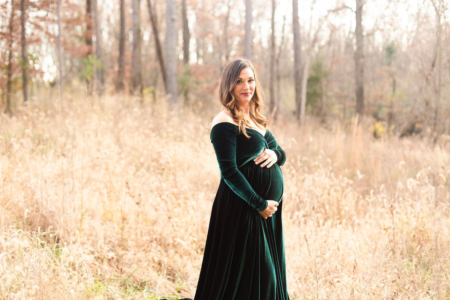 Romantic maternity portrait featuring a flowing dark green velvet gown against fall foliage.
