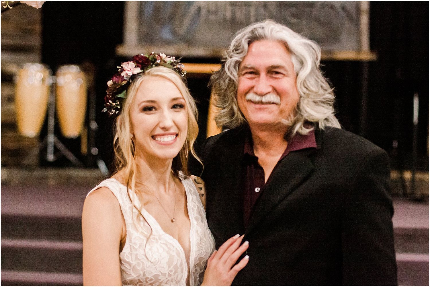 Bride in white dress poses with wedding guest against dark wooden background.