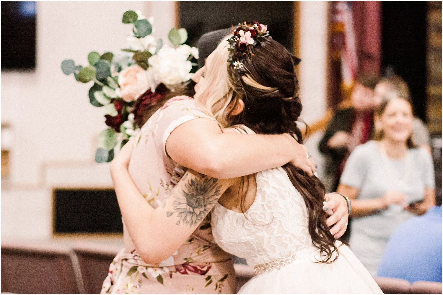 Emotional embrace between two people in formal attire at an indoor wedding celebration.