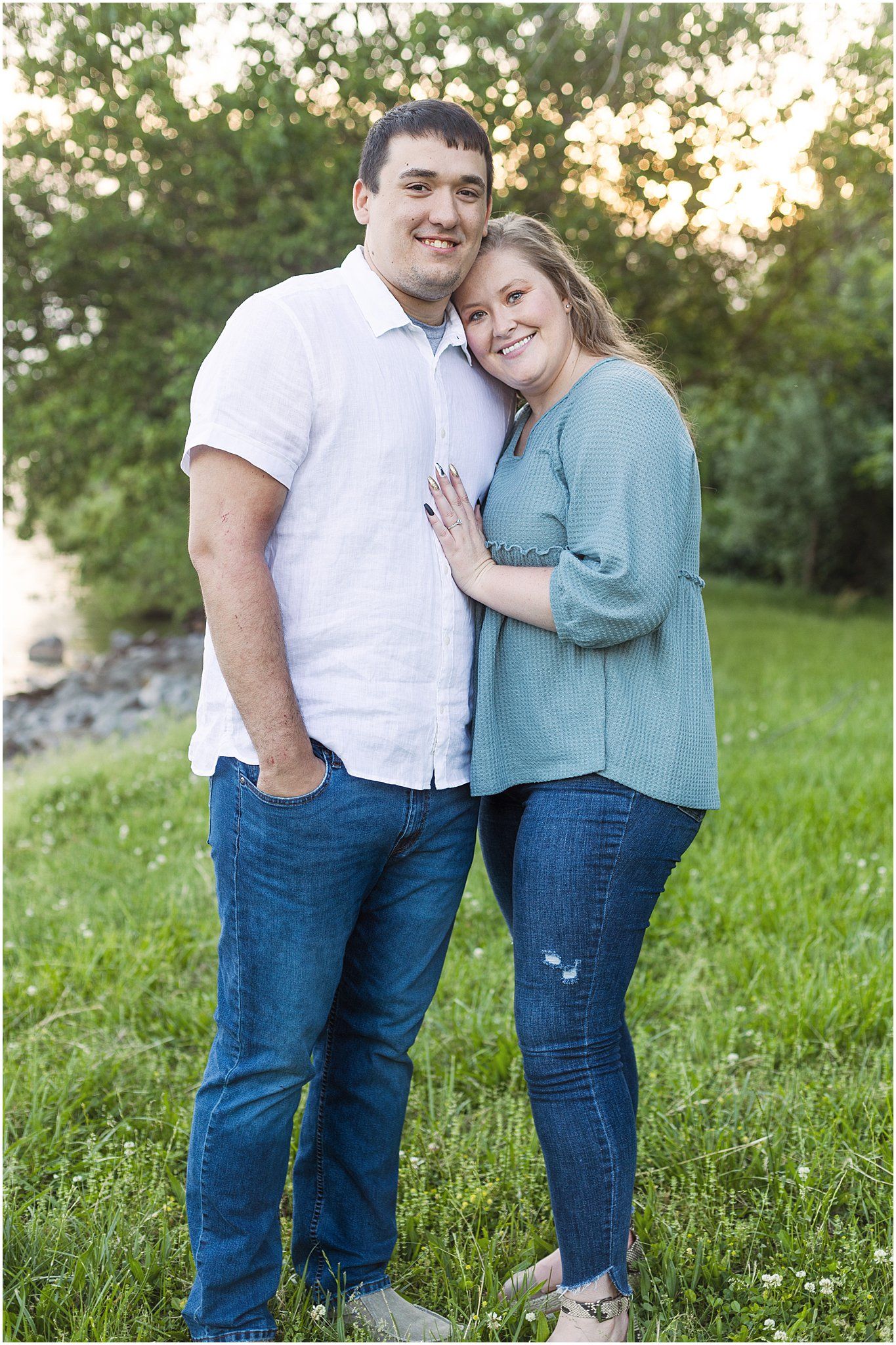 A romantic outdoor portrait of a couple standing close together on green grass with golden sunlight behind them.
