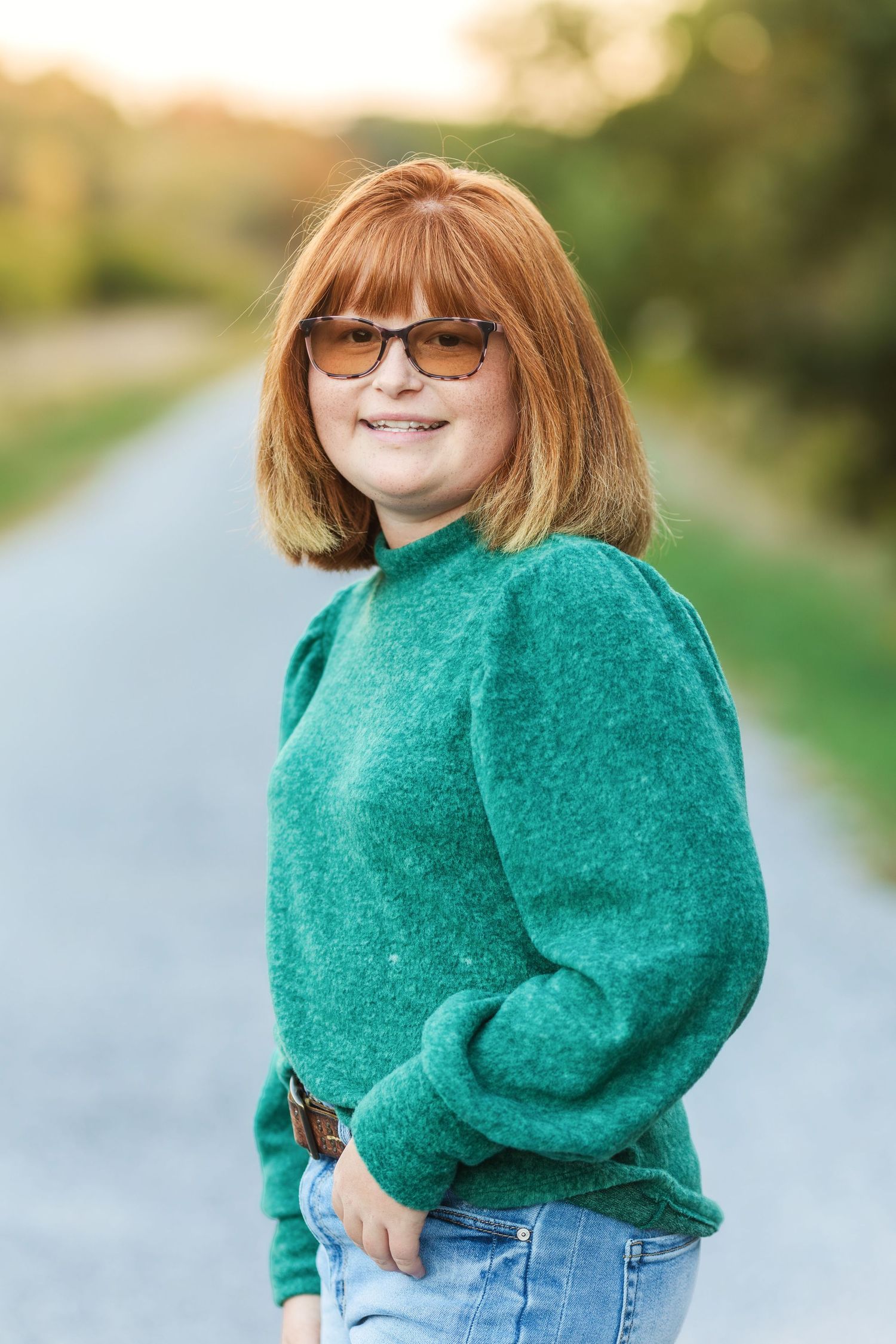 A person in an emerald green sweater poses casually on a country path.