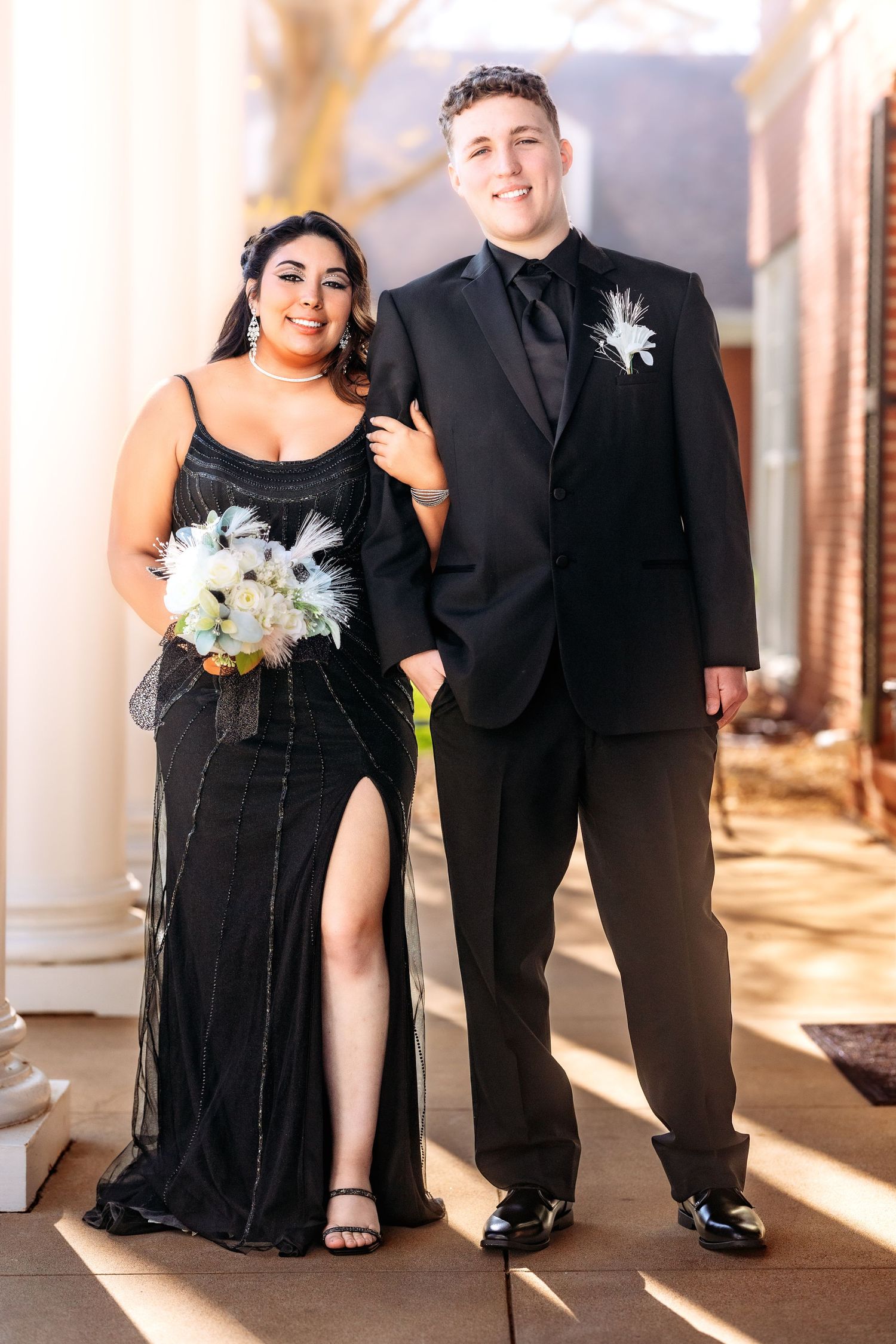 Wedding party members in black formal attire pose together in an elegant hallway with warm lighting.