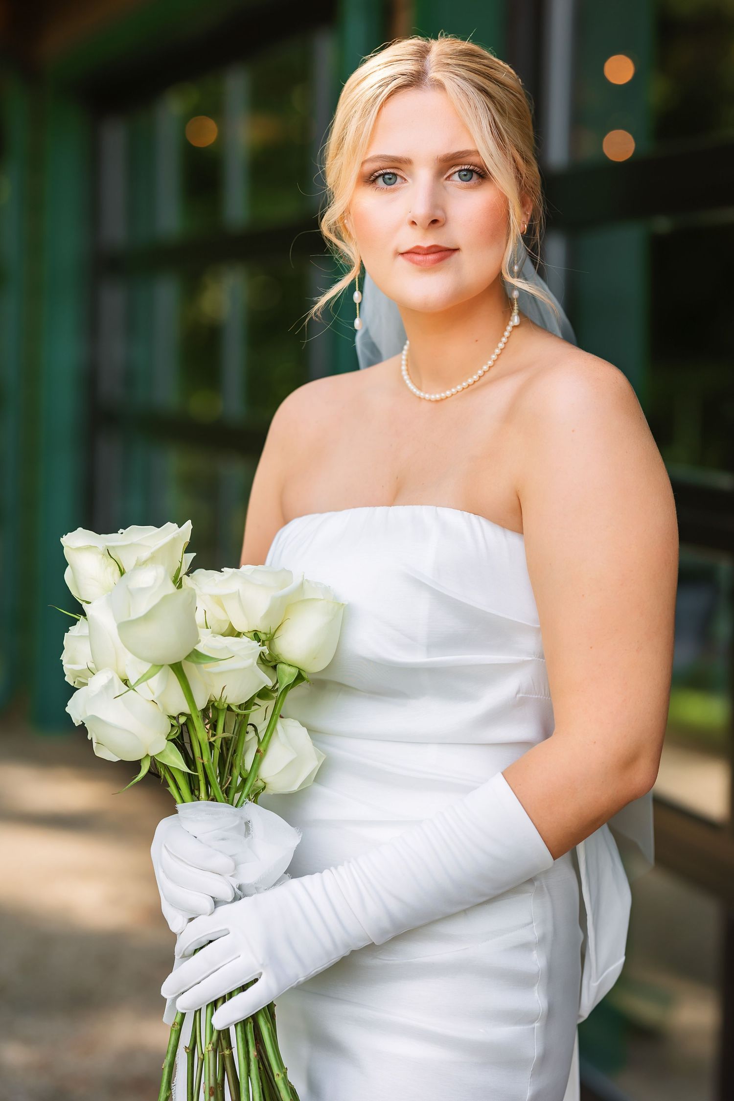 Bride in white dress holding elegant white rose bouquet and wearing long gloves.
