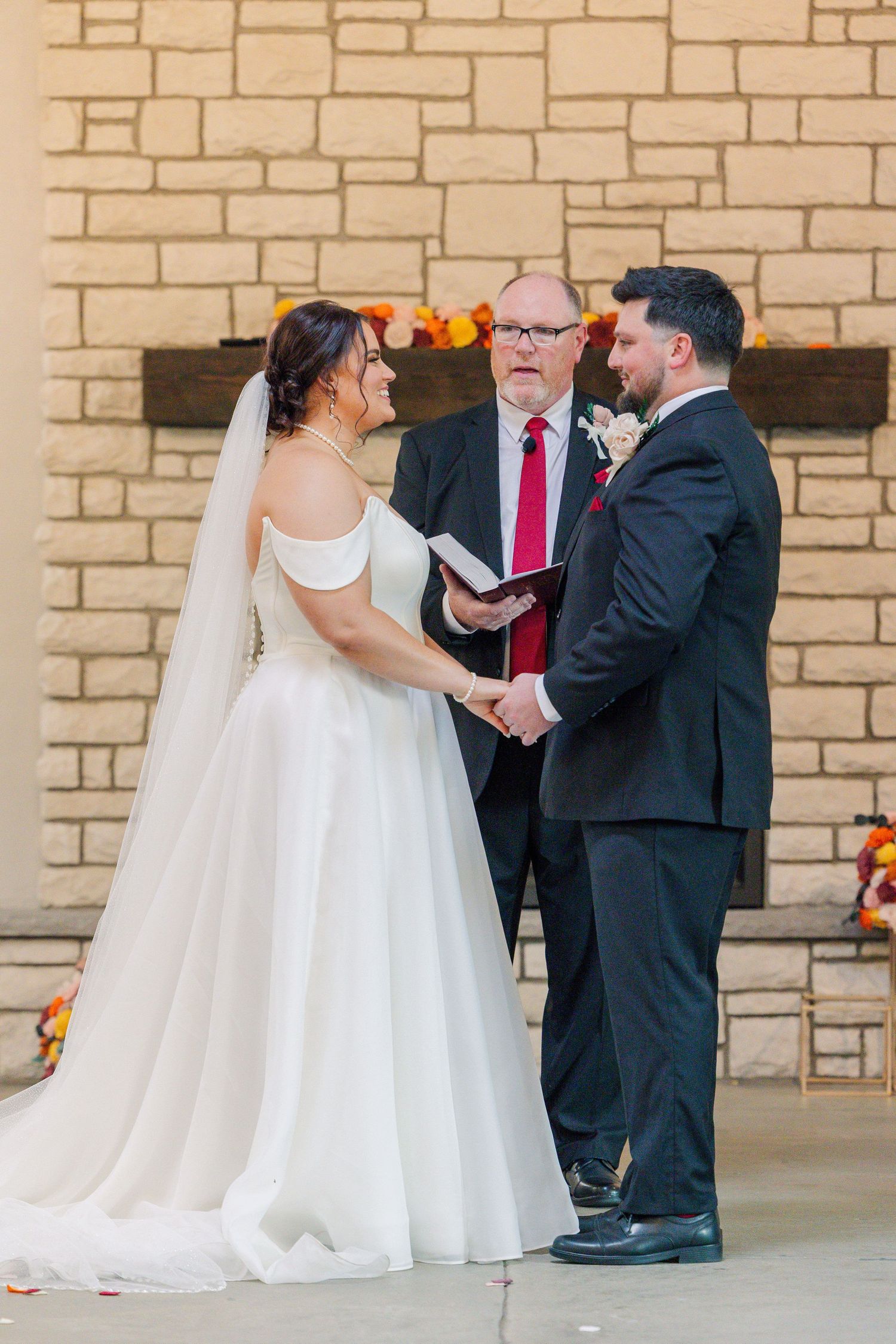 Wedding ceremony in progress against stone wall backdrop with officiant holding ceremony book.