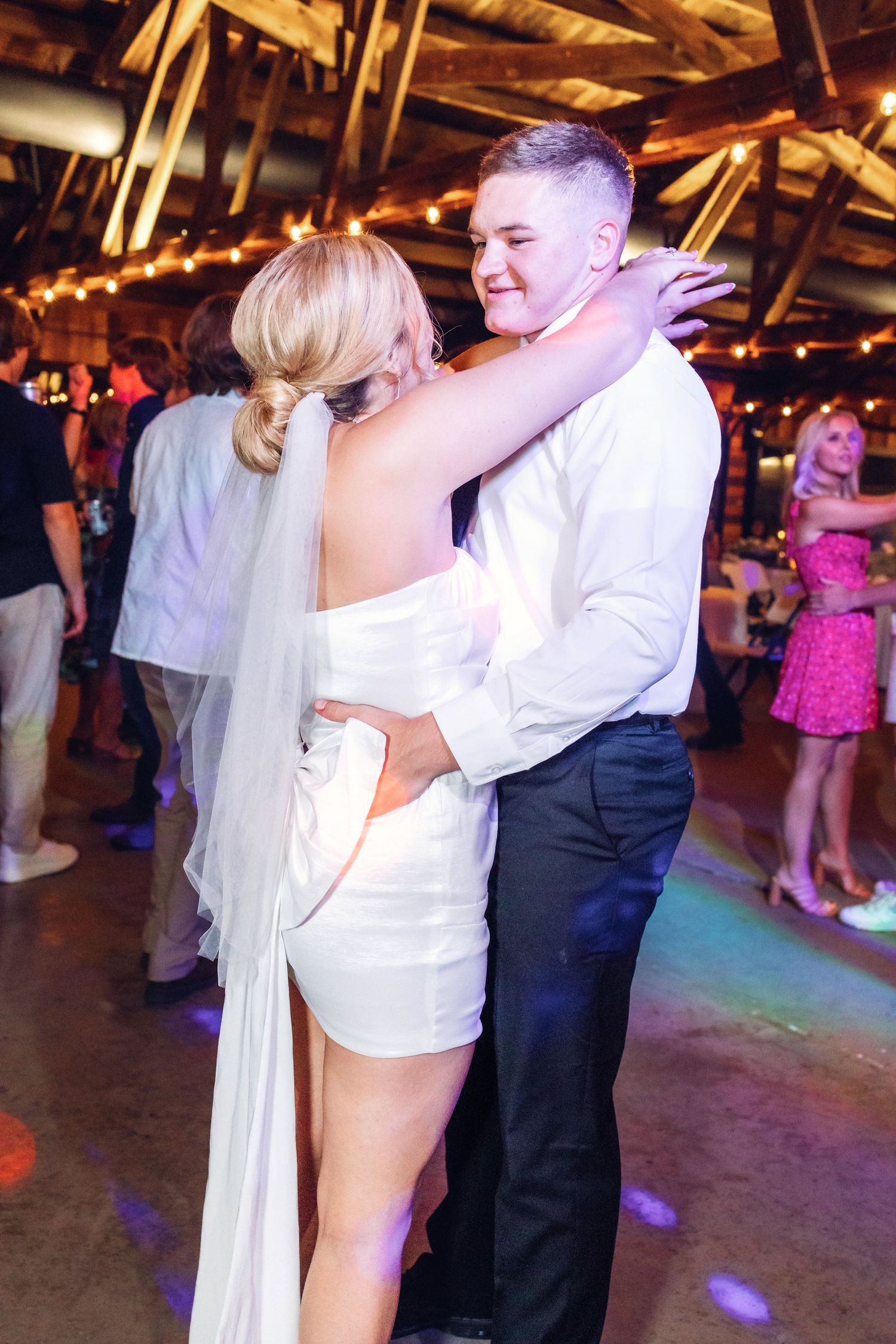 Wedding guests dancing and celebrating on a dimly lit dance floor with colorful lighting.