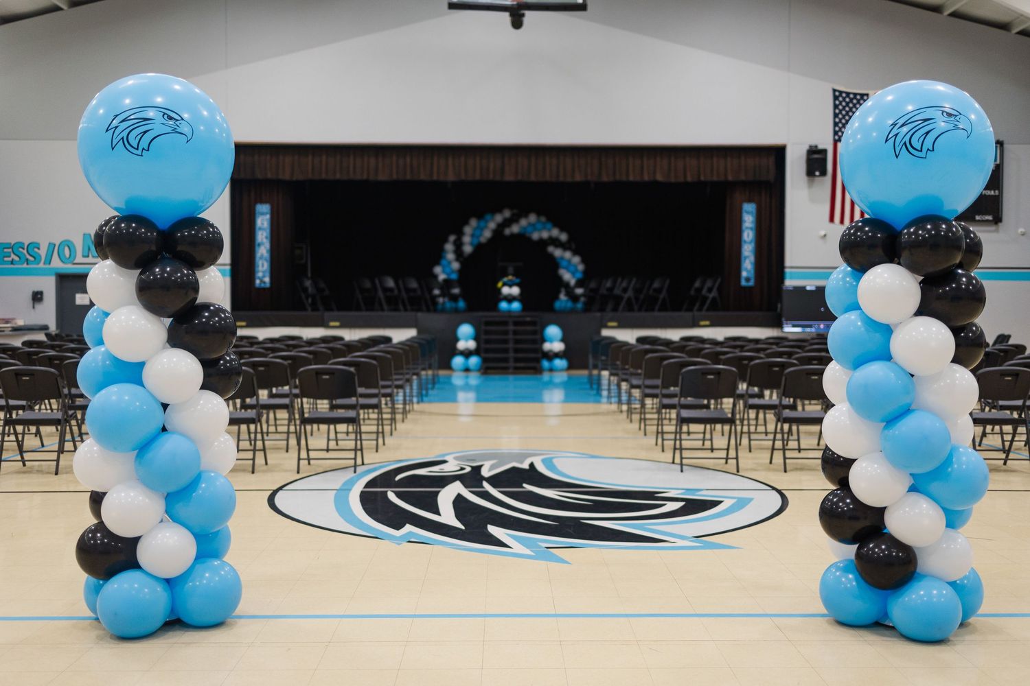 Indoor graduation venue with rows of chairs and blue balloon decorations.