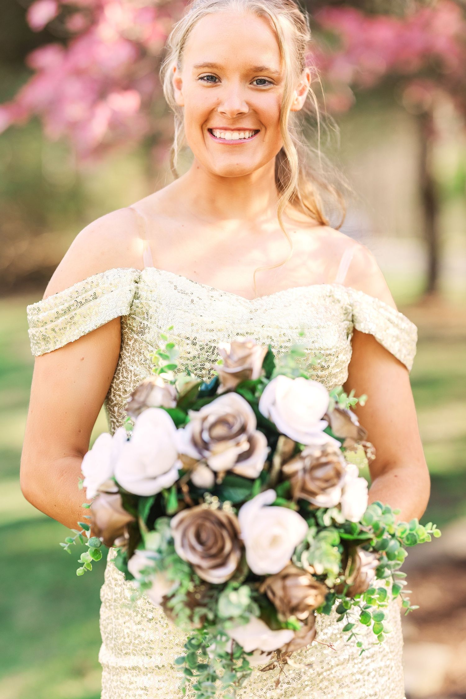 Person in sparkly gold dress holding a white and green floral bouquet outdoors.
