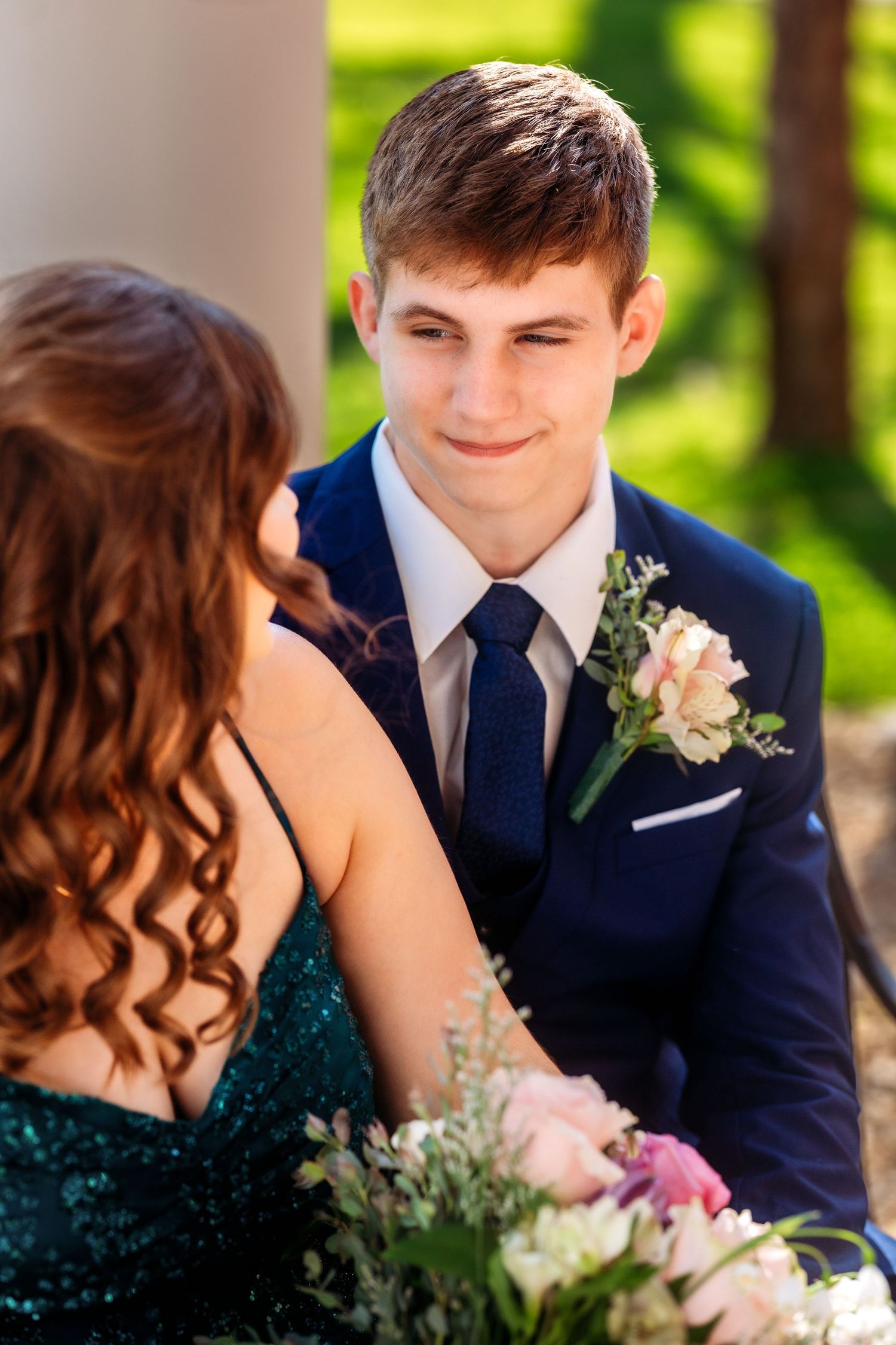 A couple in formal attire share an intimate moment at a prom or formal dance with pink and white floral accents.