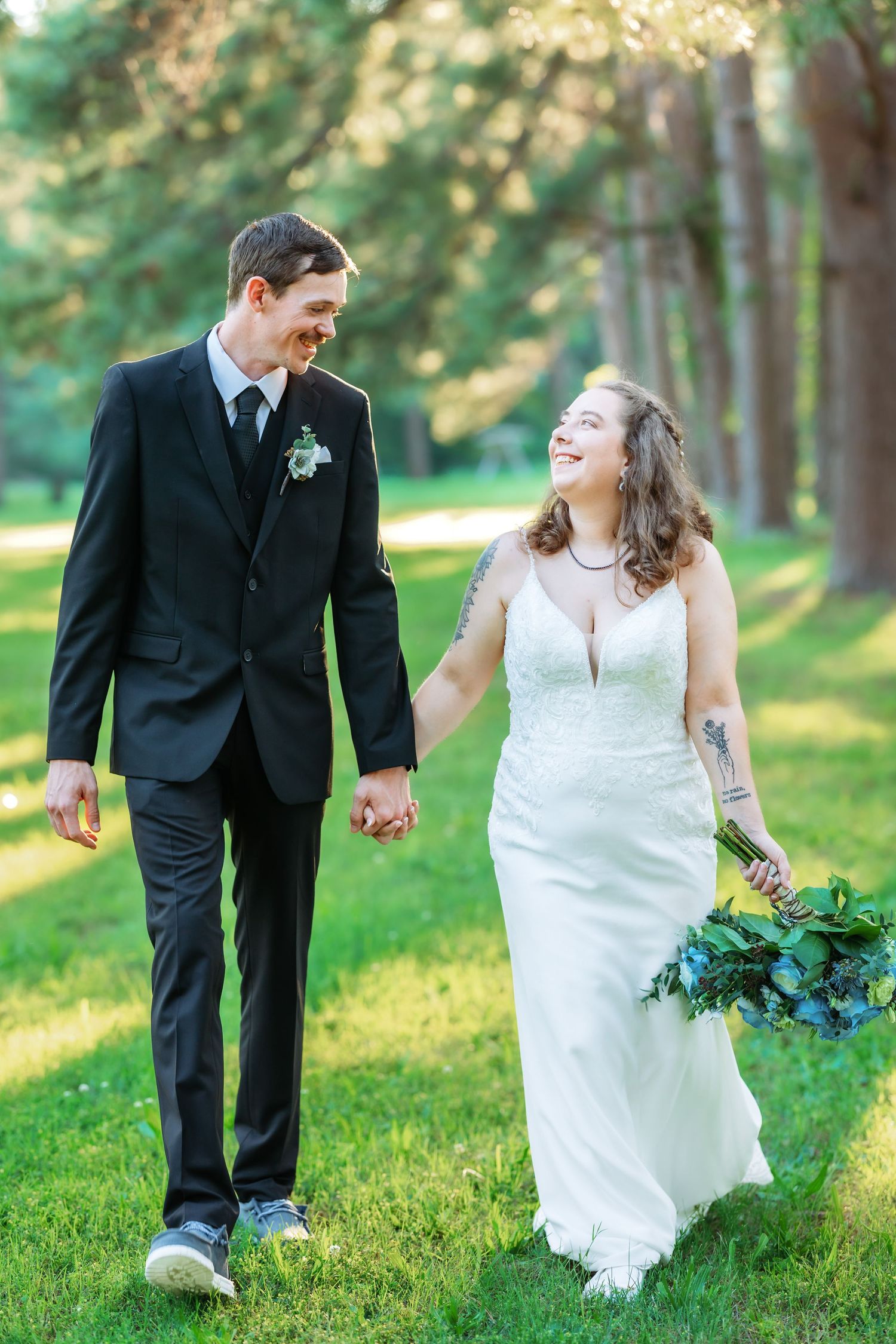 Joyful wedding couple walking hand in hand through sunlit wooded area.