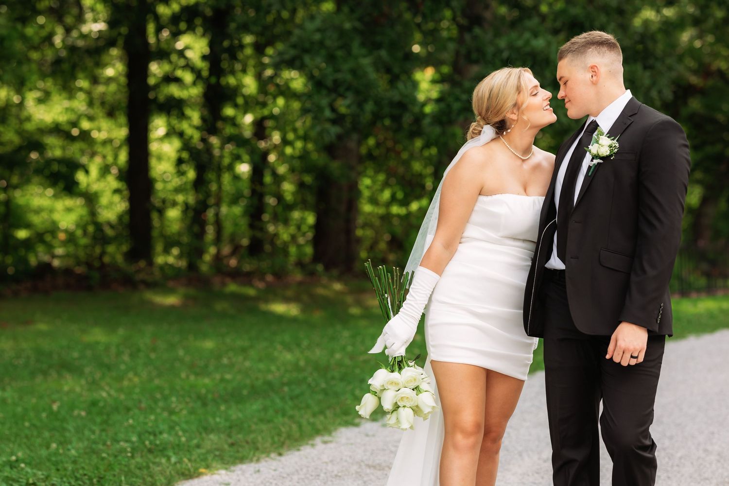 Wedding couple shares romantic moments on an outdoor path with green foliage backdrop.