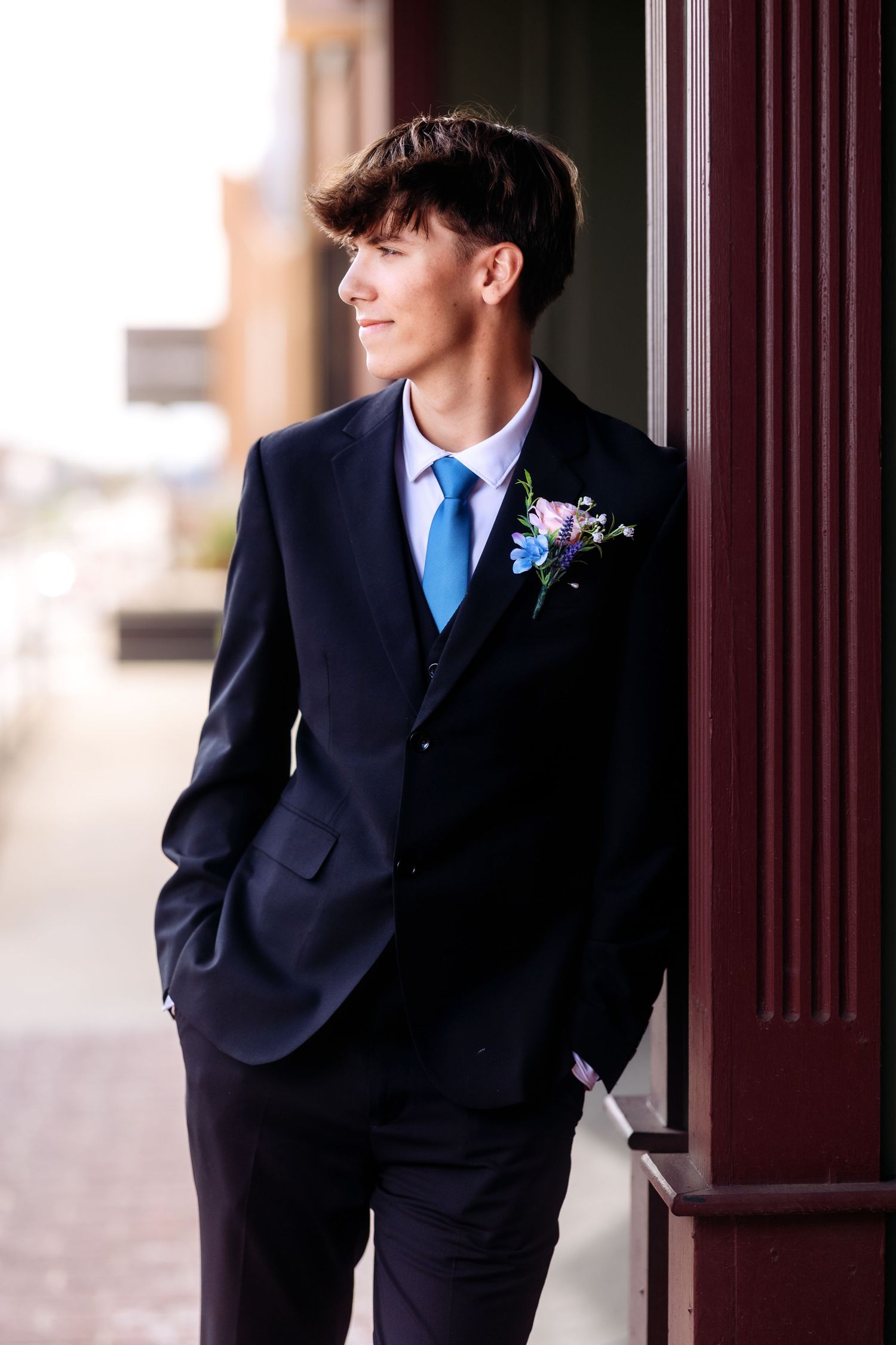 Classic navy suit with blue tie and boutonniere against architectural columns.