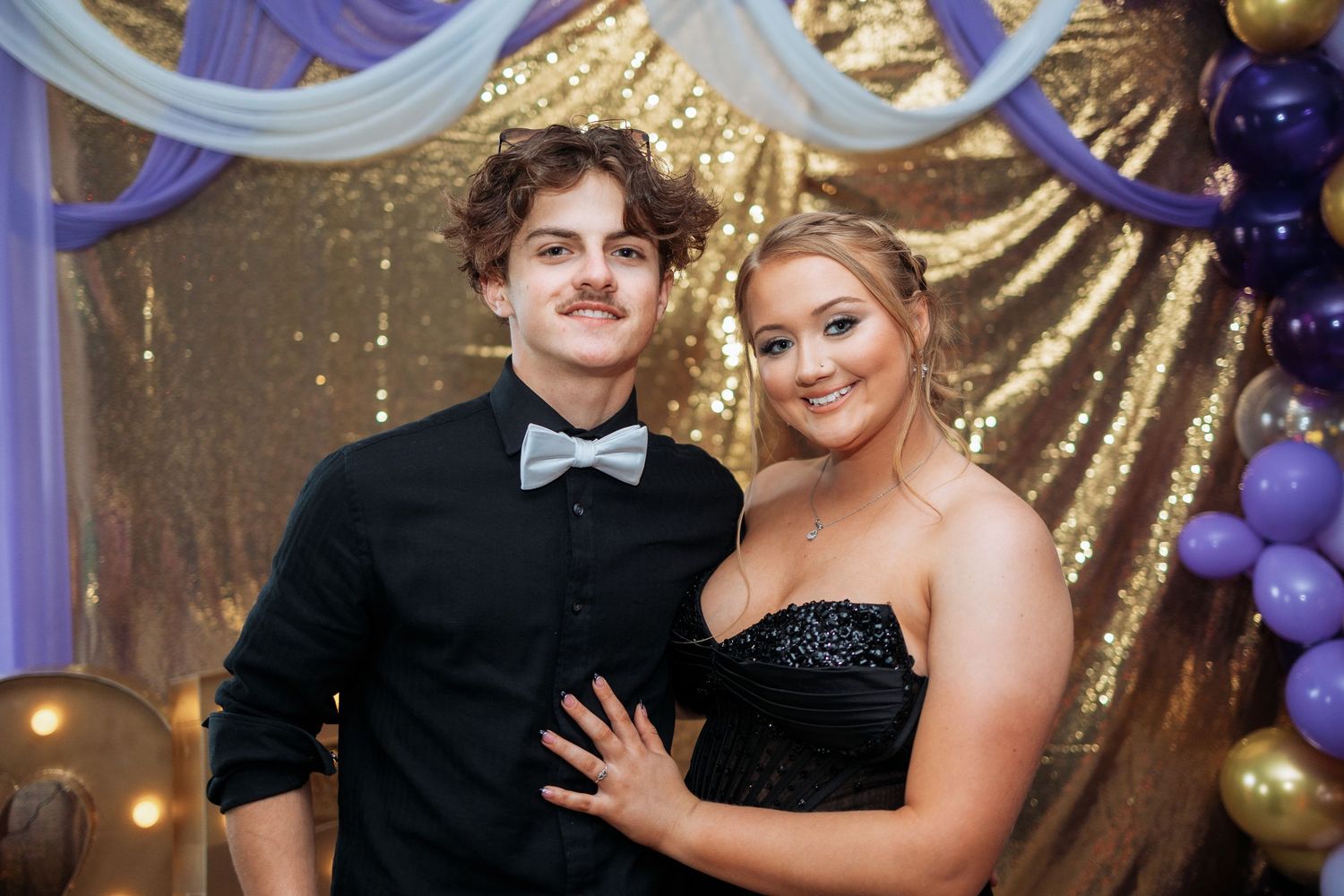 Couples dancing together at a formal event with gold and purple decorations in the background.