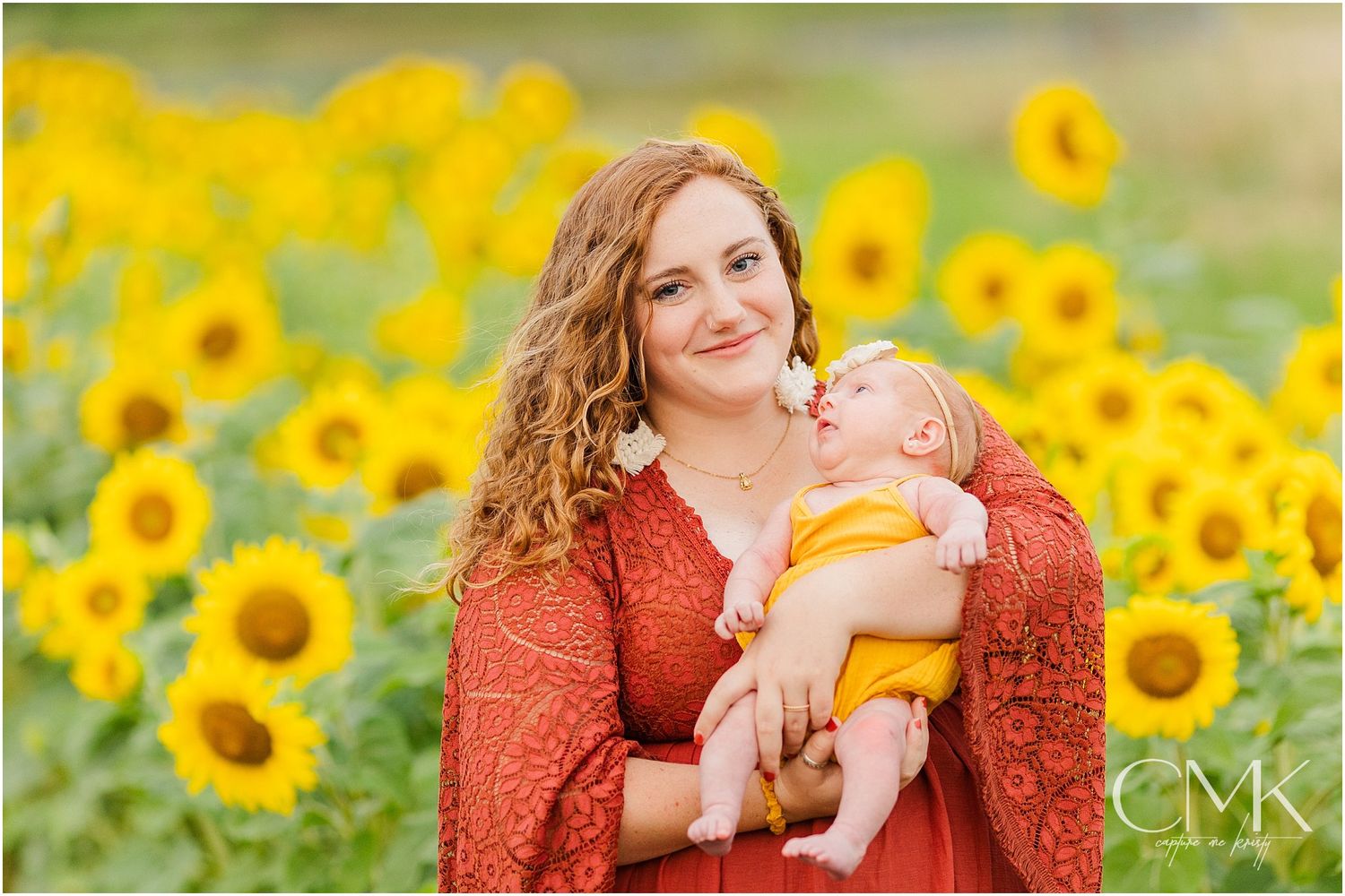 Mother and baby share sweet moment in field of bright yellow sunflowers.