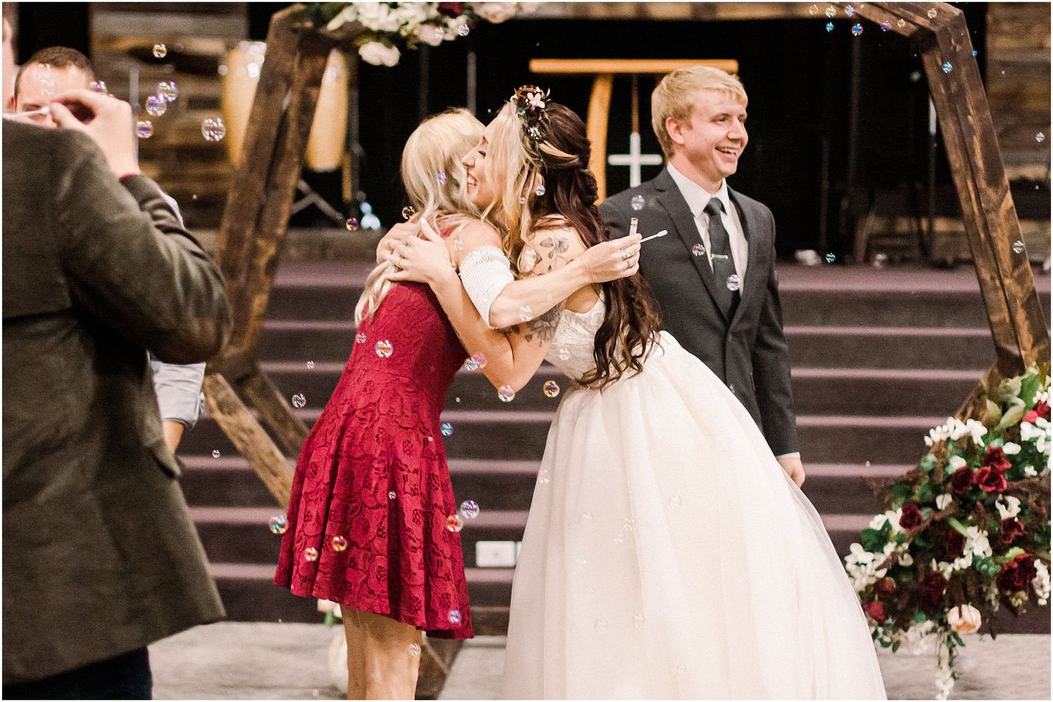 A wedding celebration where guests share a joyful moment near stairs decorated with floral arrangements.