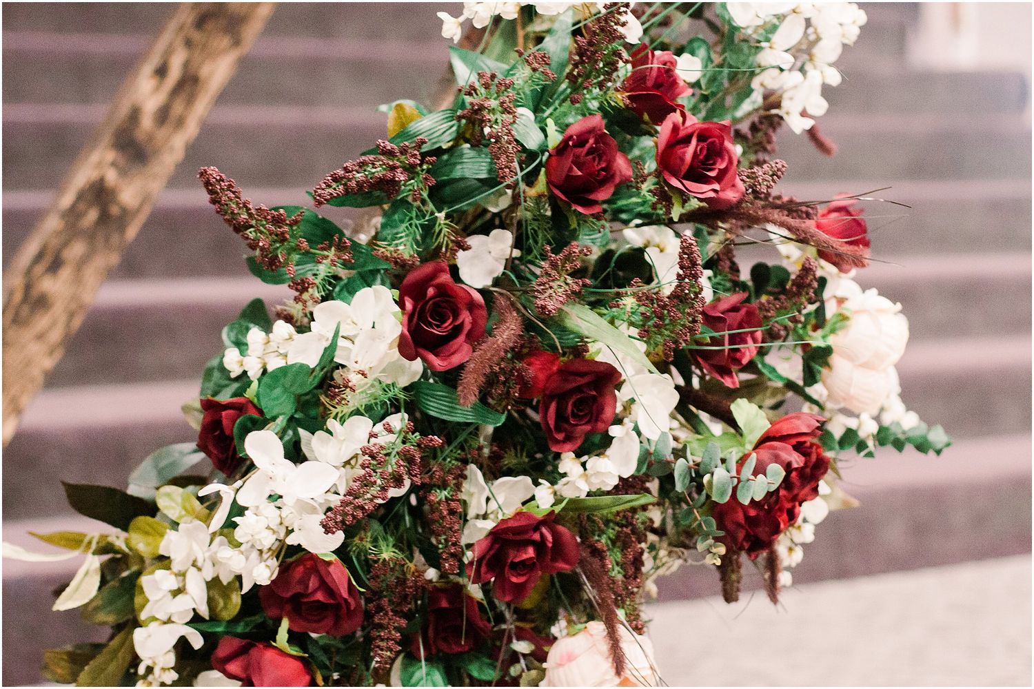 Stunning burgundy and white floral arrangement with roses and greenery on wooden ladder.
