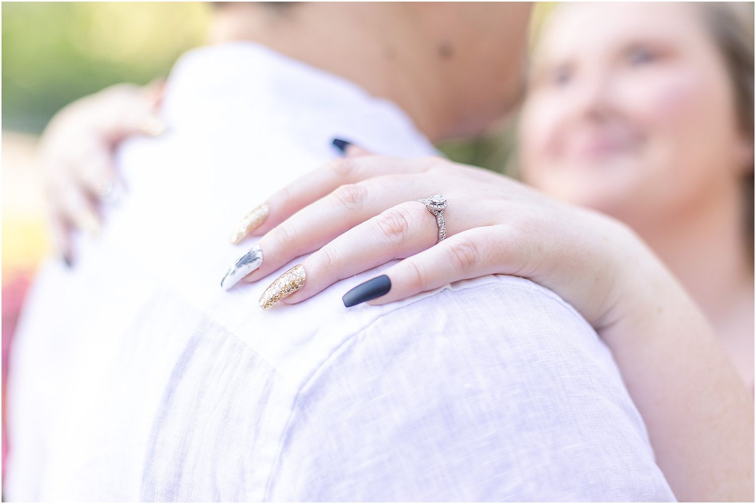 Close-up of engagement ring and navy nail polish against white shirt.