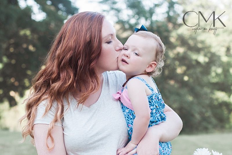Tender moment captured between woman in white and child in blue dress against outdoor background.