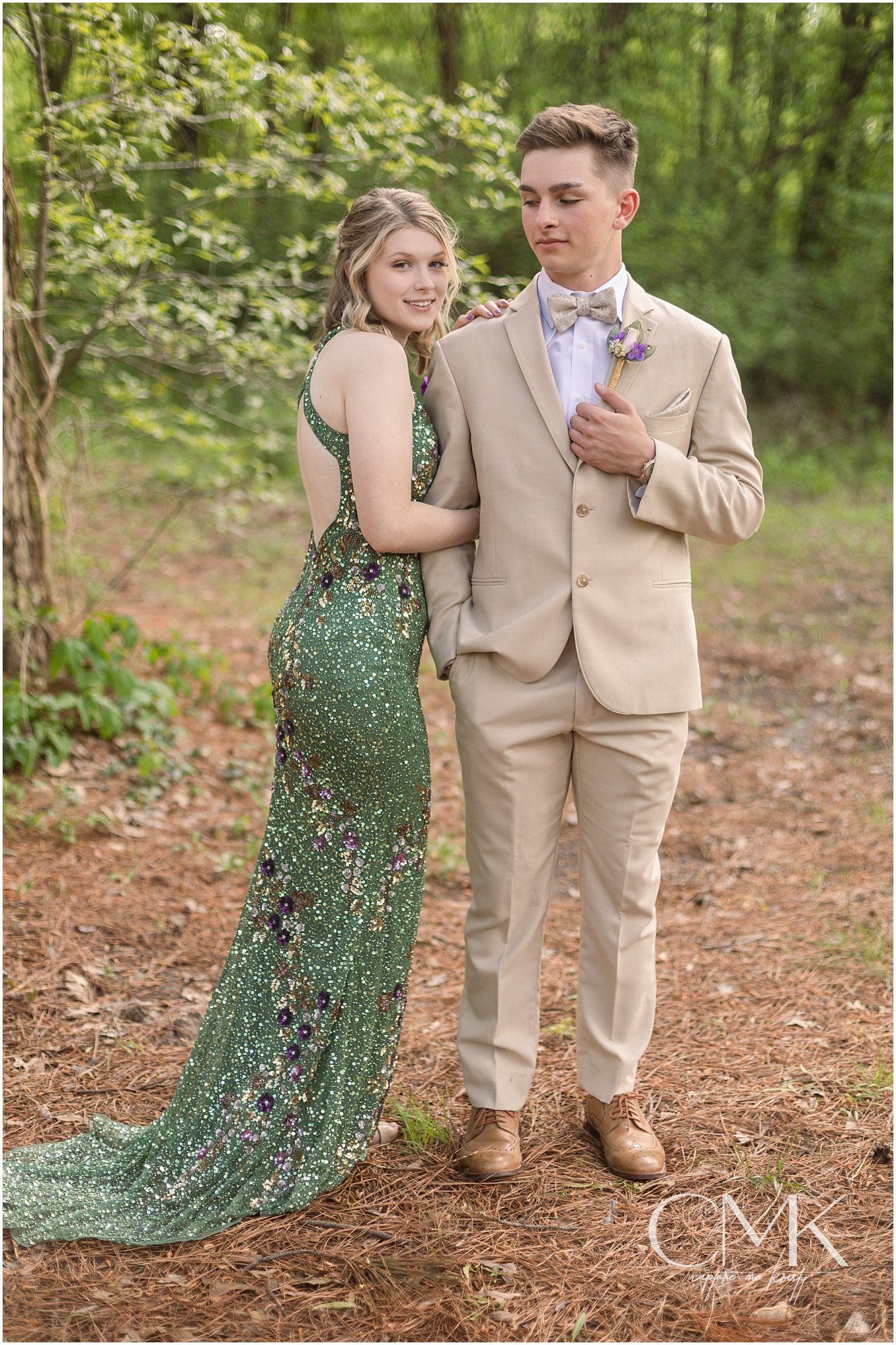 A couple shares a romantic moment in formal attire against a forest backdrop.