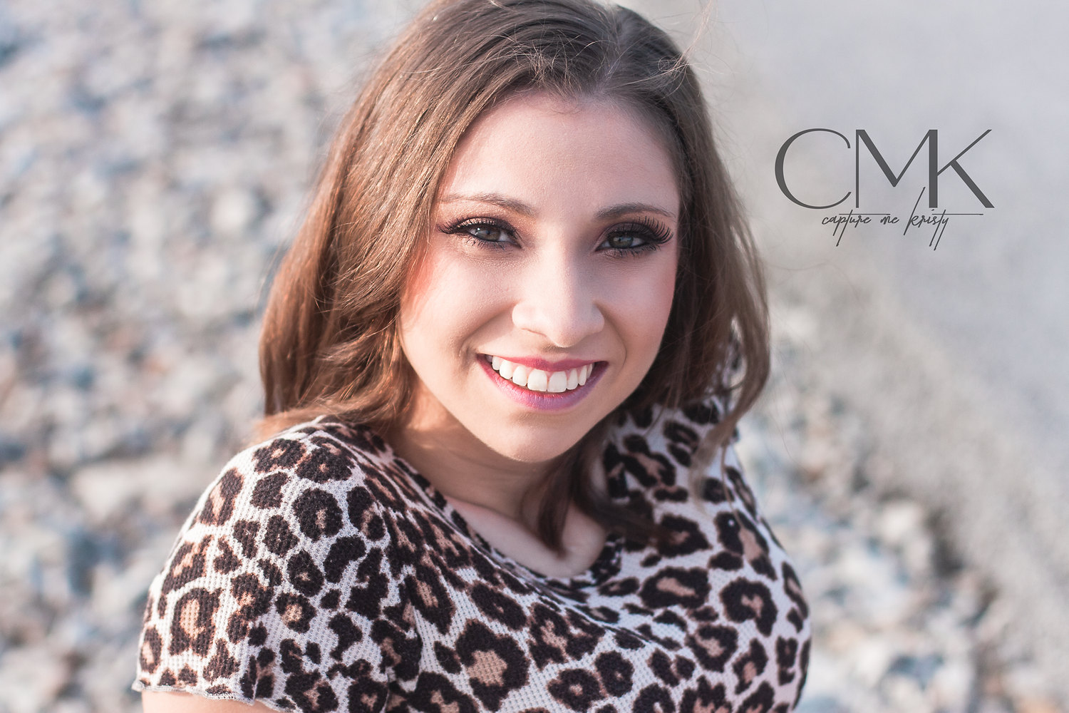 Close-up outdoor portrait featuring leopard print top and natural lighting by rocky shore.