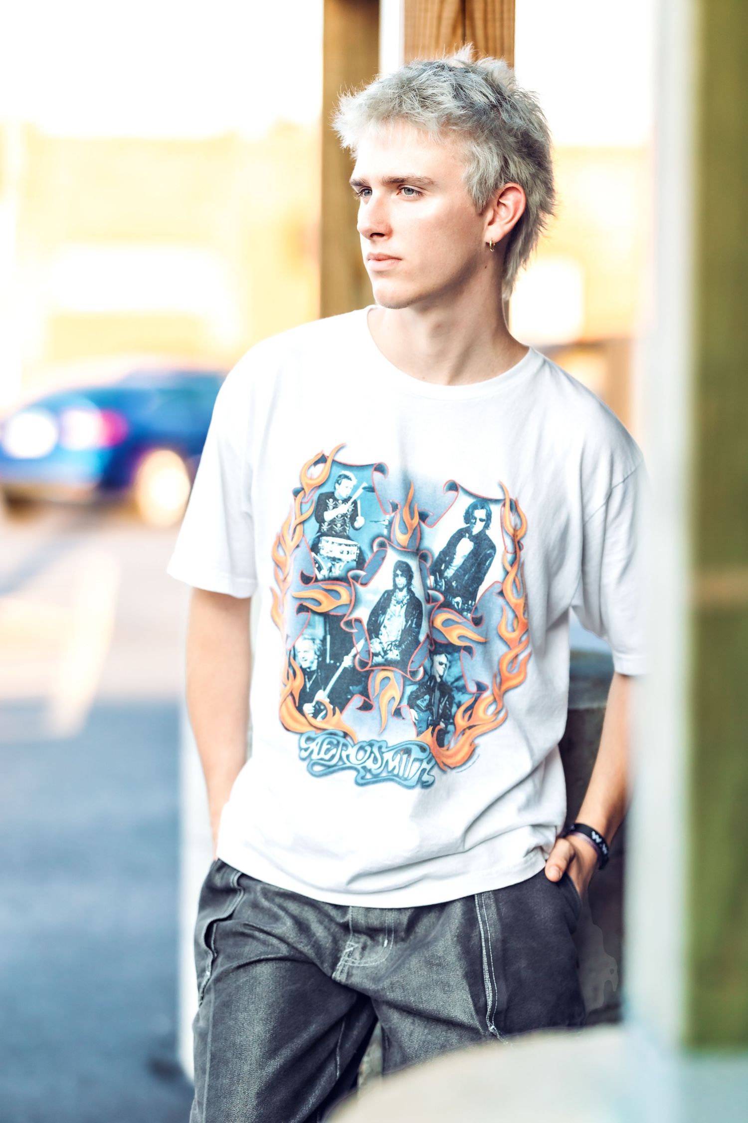 Individual wearing graphic t-shirt and jeans stands near pillars in urban setting.