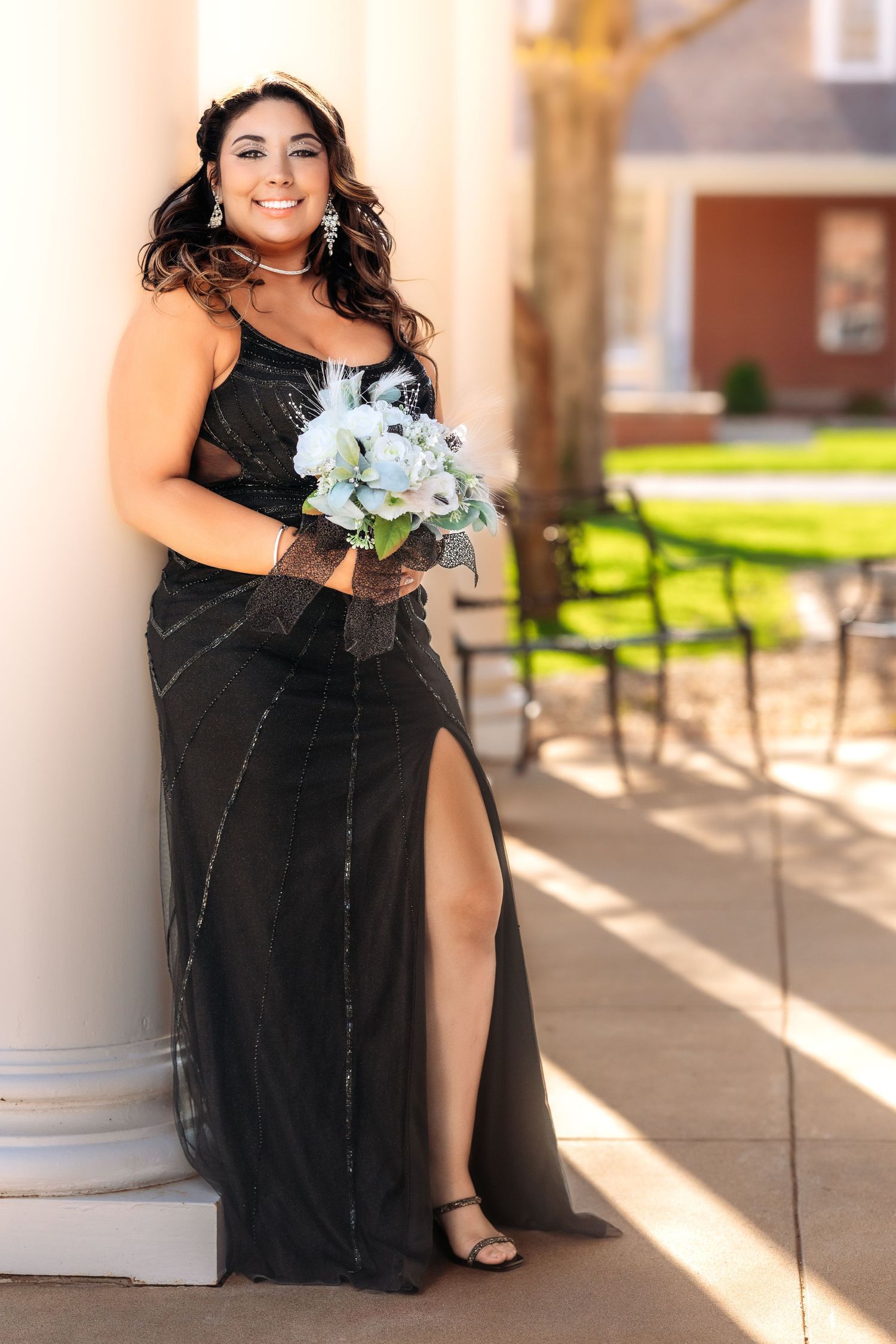 A person in a black dress holds a bouquet of white flowers while sitting on outdoor steps in warm sunlight.