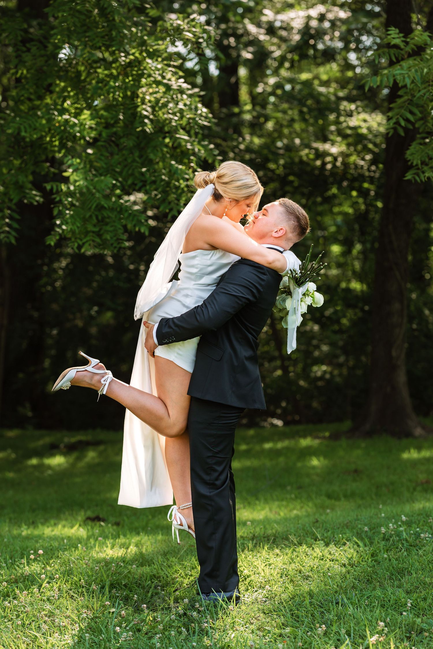 Romantic dip kiss between newlyweds on grassy lawn.