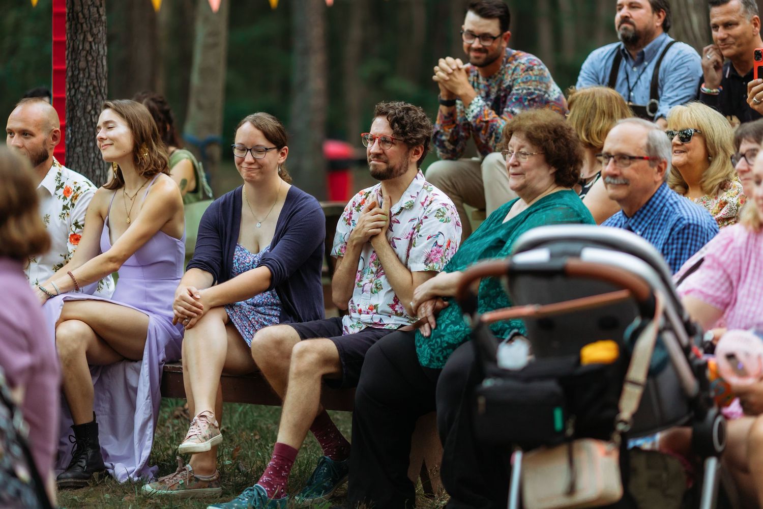 Wedding guests seated outdoors watching the ceremony with colorful decorative bunting overhead.