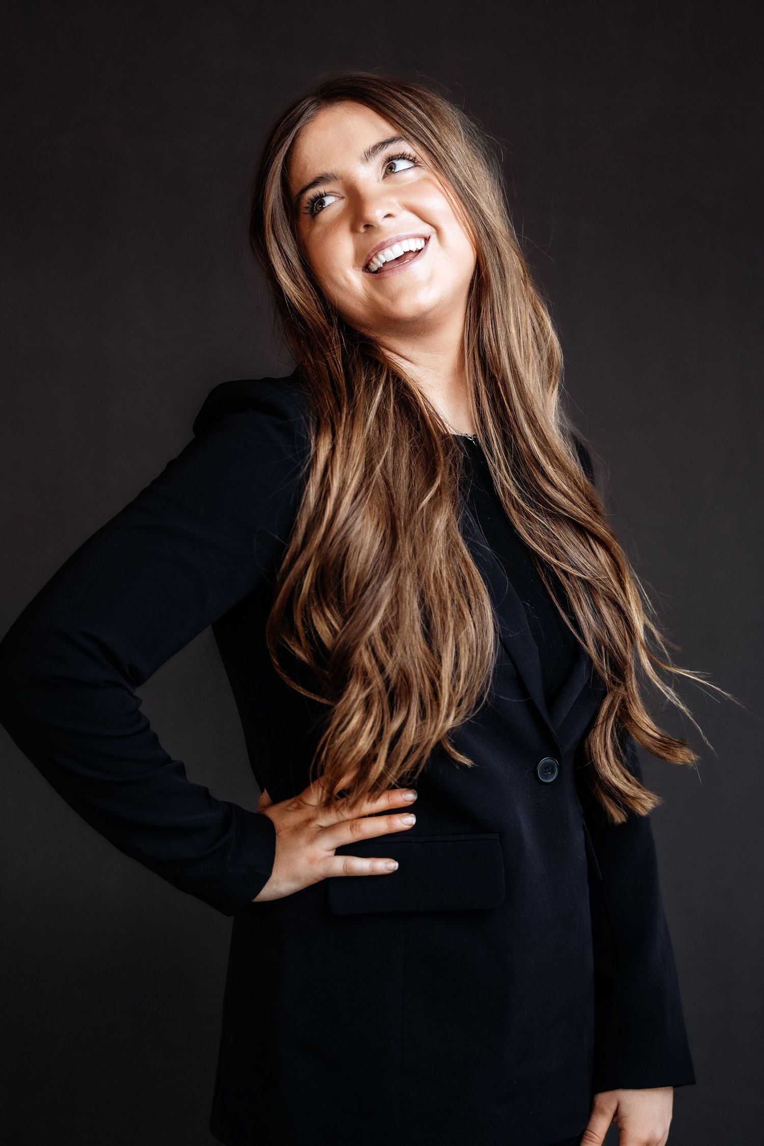 Dynamic portrait of a person in black blazer posing against dark background.