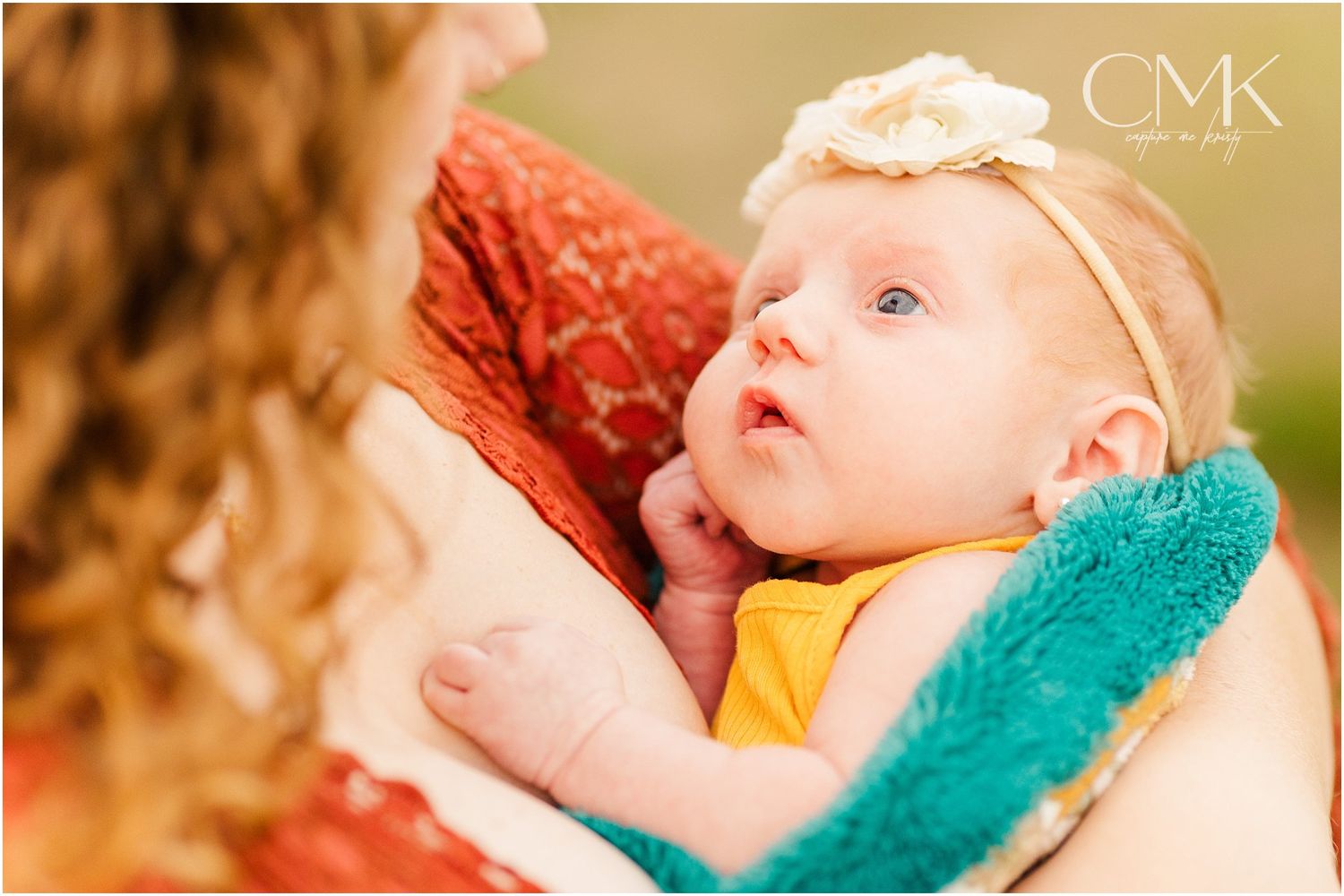 Close-up shot of infant wearing headband while being held against rust-colored clothing.