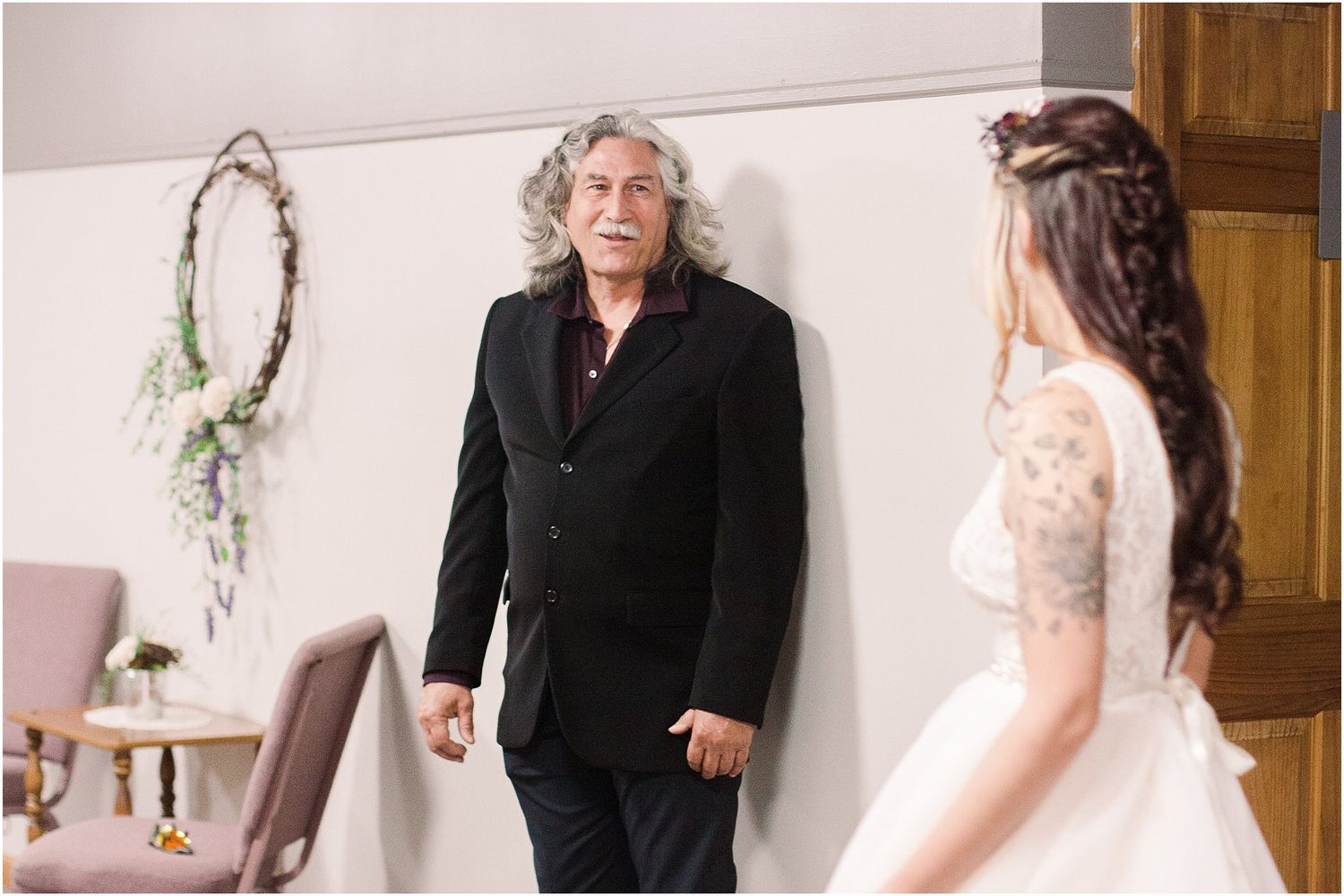 A touching first look between a bride in a lace gown and a person in black at an indoor venue.
