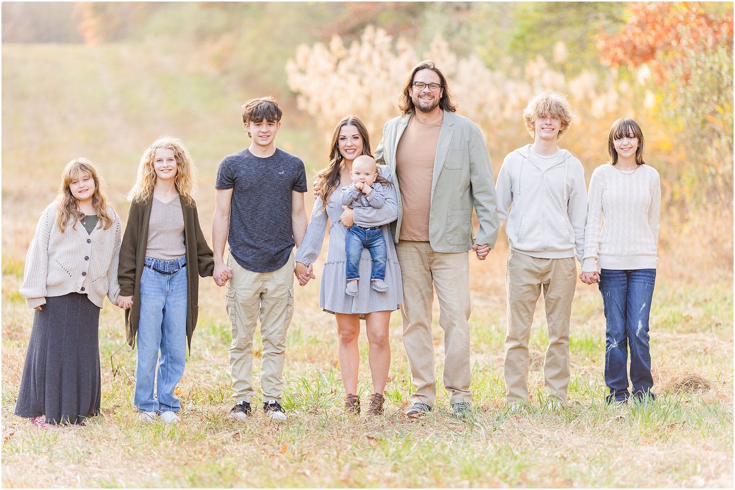 Casual family group portrait in autumn field wearing coordinated neutral colors.