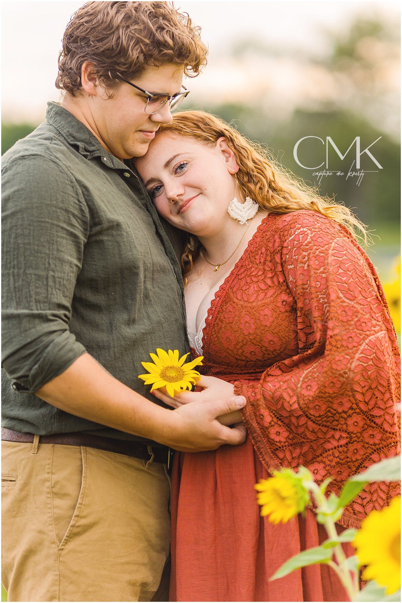 A tender embrace captured among blooming sunflowers with a sunflower held between them.