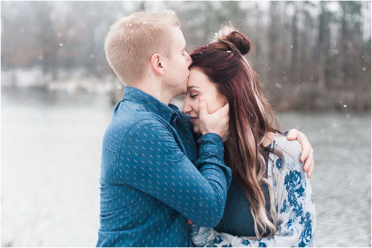 An intimate winter portrait captures a couple in blue sharing a close embrace by a lake.