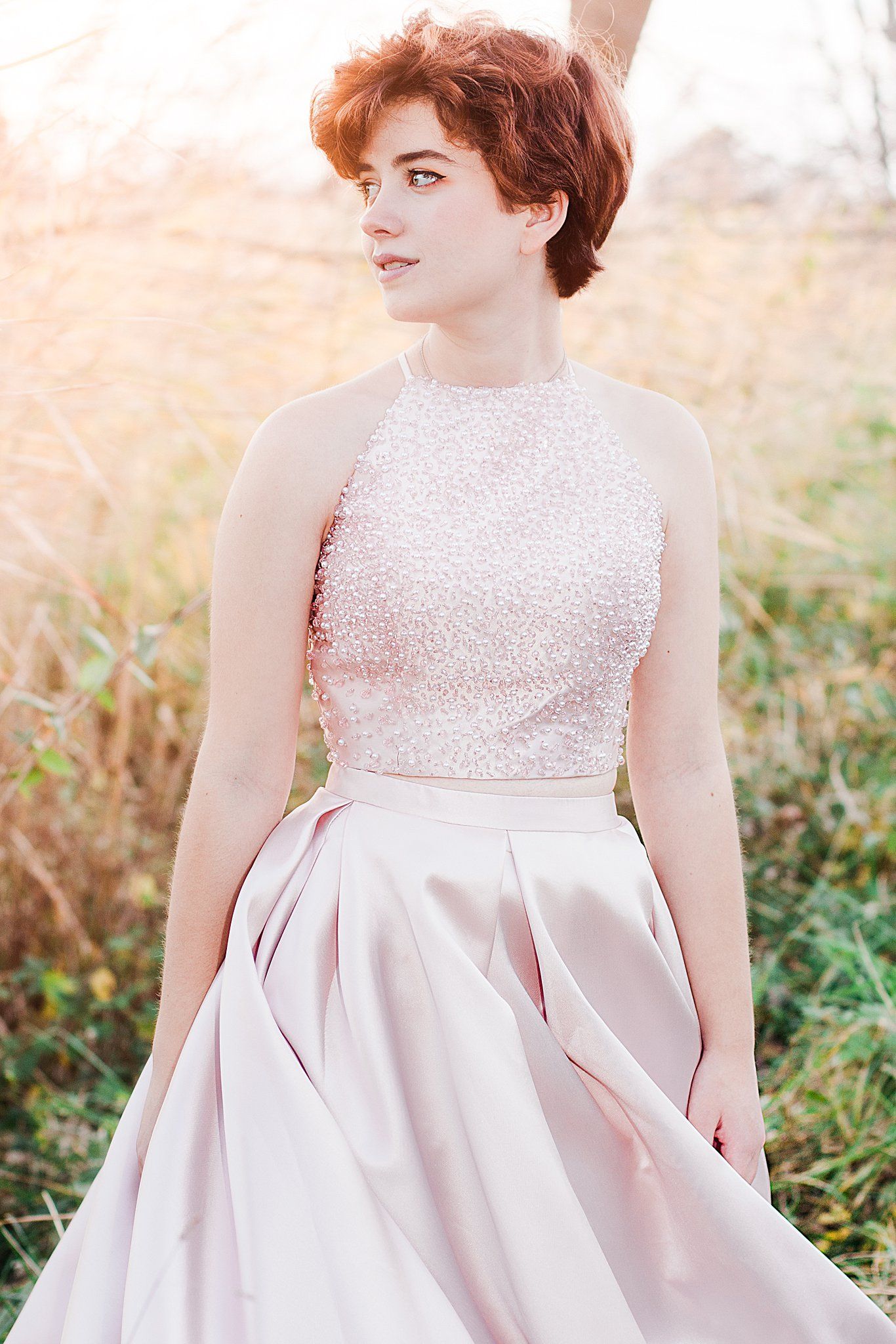 Person wearing sparkly pink formal dress poses in golden field at sunset.