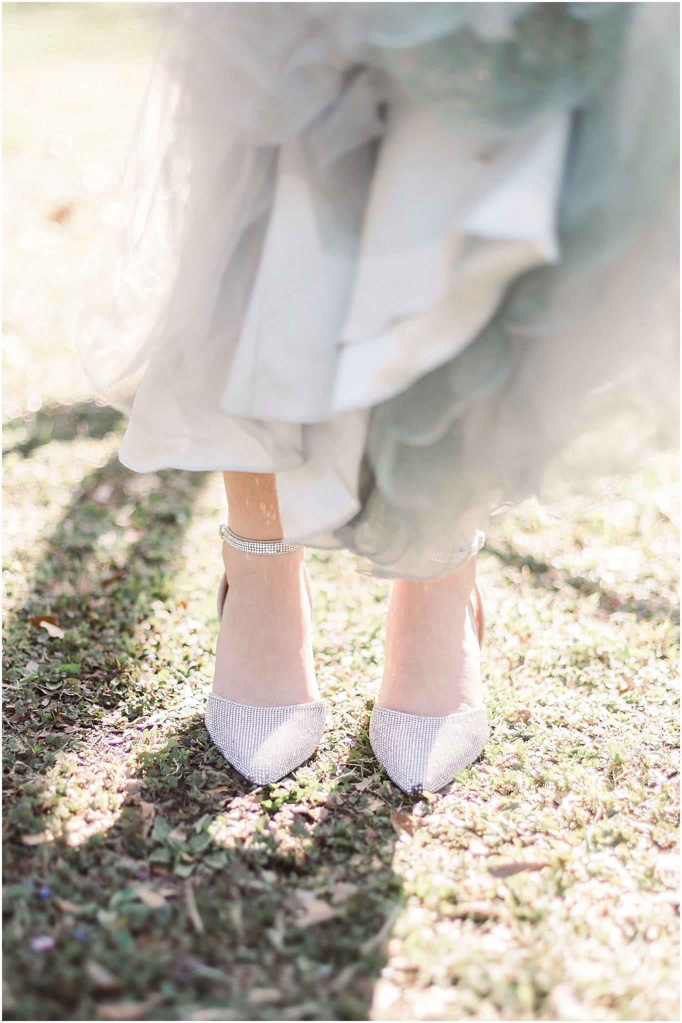 Close-up of delicate white pointed heels and an anklet on grass in soft lighting.