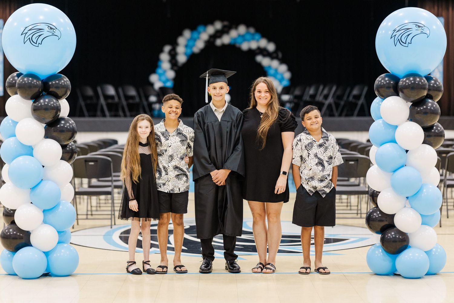 Graduation celebration with blue and white balloon arches and family group photo.