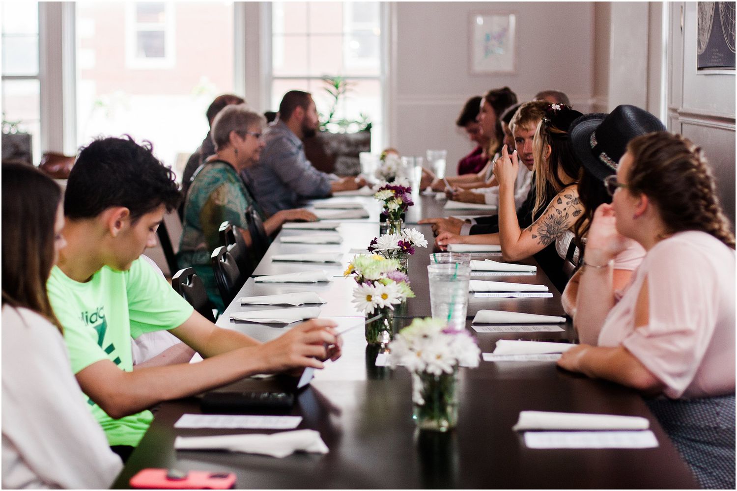 People seated at a long dining table with place settings and floral centerpieces during an event.