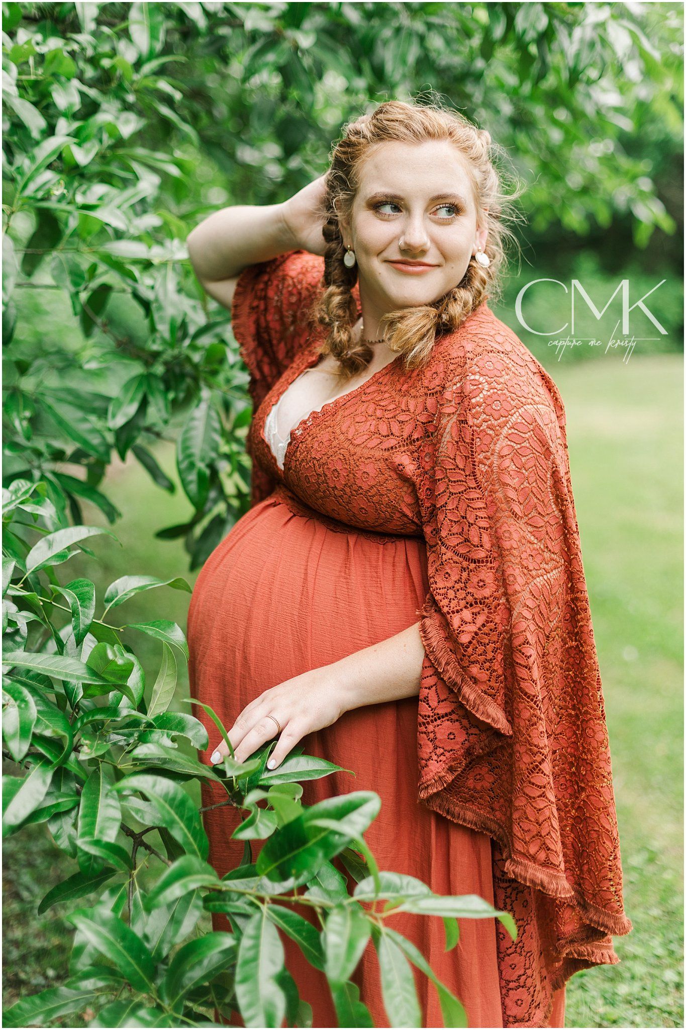 A pregnancy photoshoot features an expectant mother in a flowing coral dress posed against greenery.