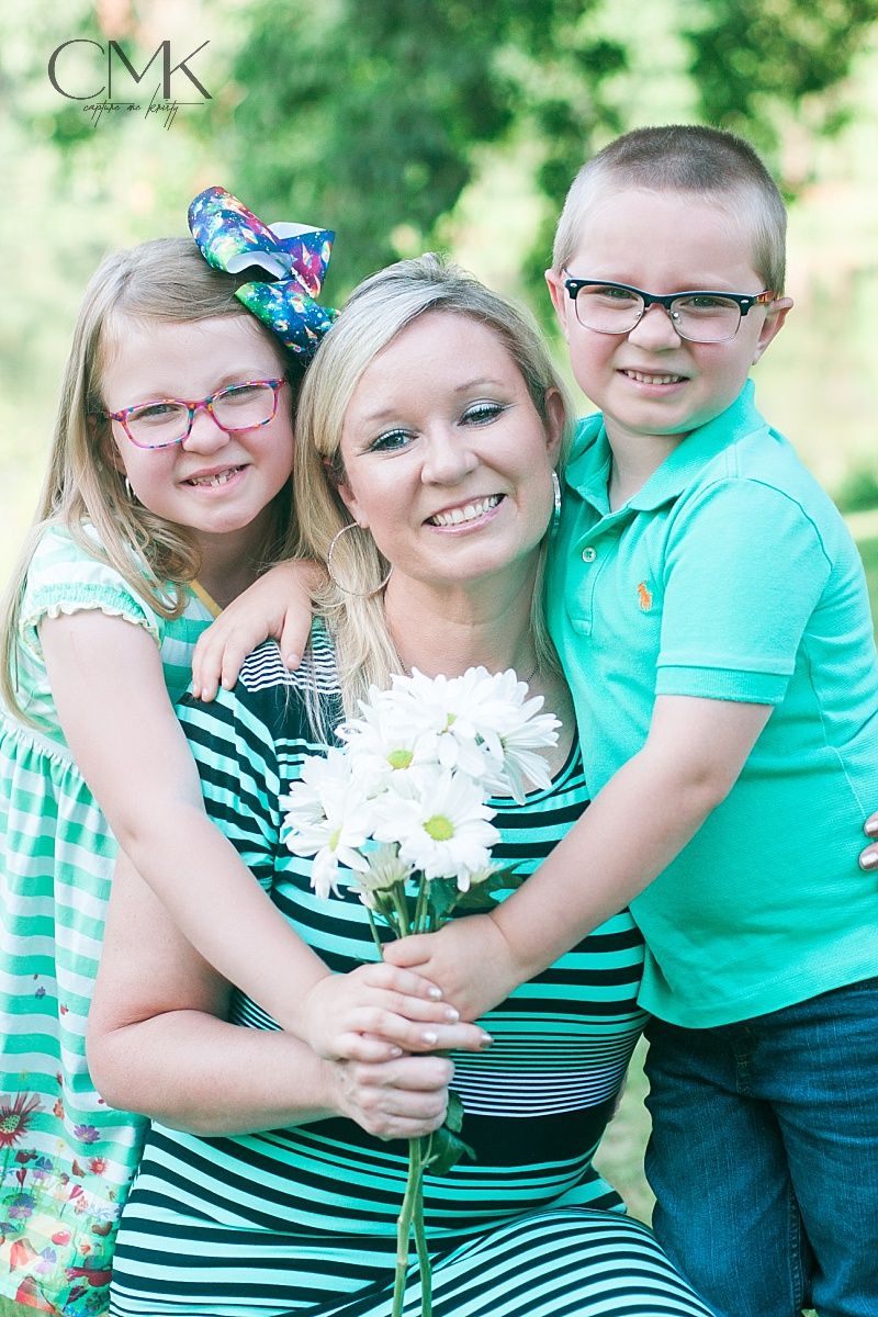 Three people wearing coordinated mint green and striped outfits pose together with white daisies in an outdoor setting.