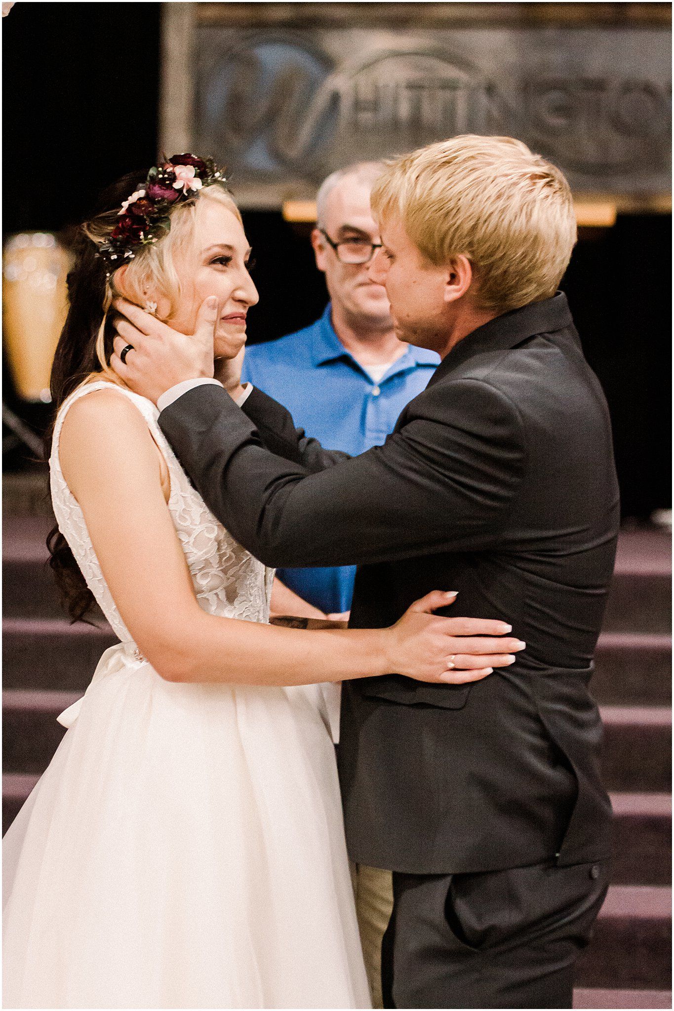 A sweet embrace between bride and groom during their wedding ceremony with an officiant in blue.