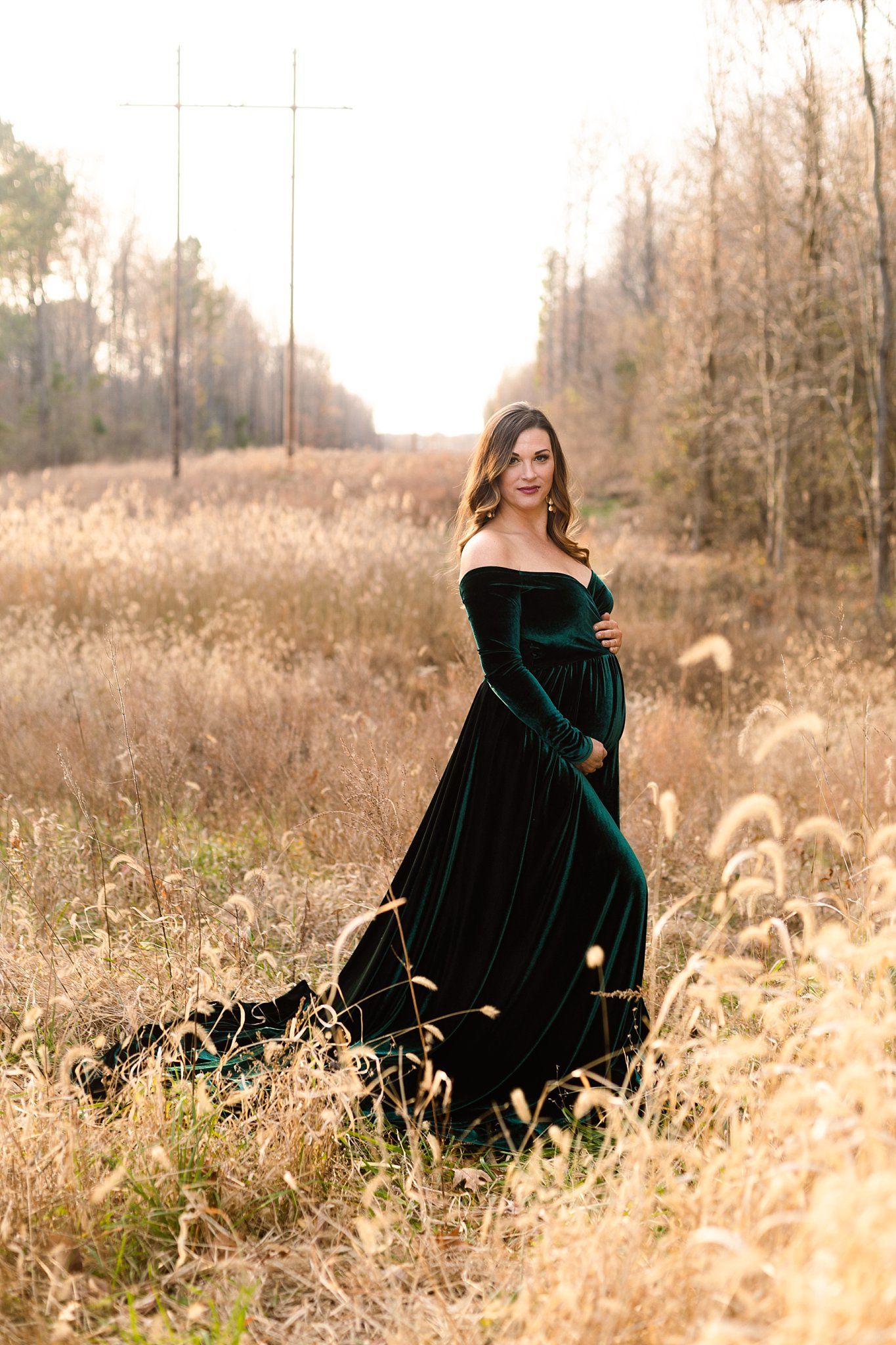 Long emerald velvet dress contrasts beautifully with autumn field and misty forest background.