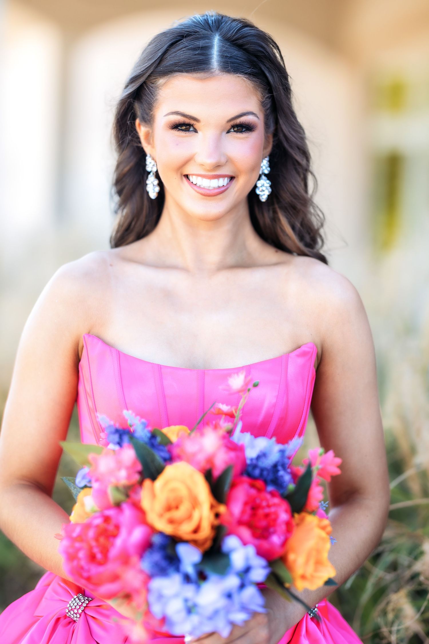 Woman in bright pink strapless gown holds vibrant bouquet with orange roses and blue hydrangeas.