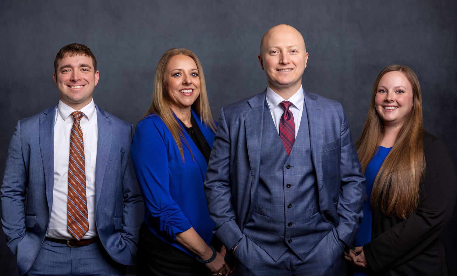 Professional business team poses together in formal attire against dark studio background.
