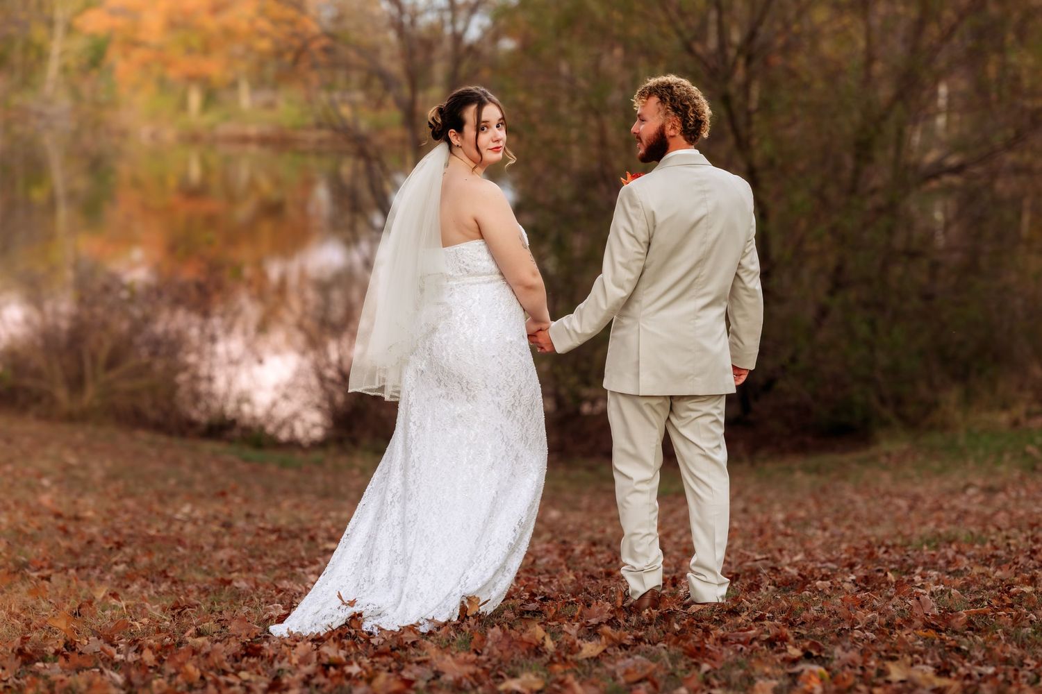 Wedding couple walking hand in hand through a forest covered in fallen autumn leaves.
