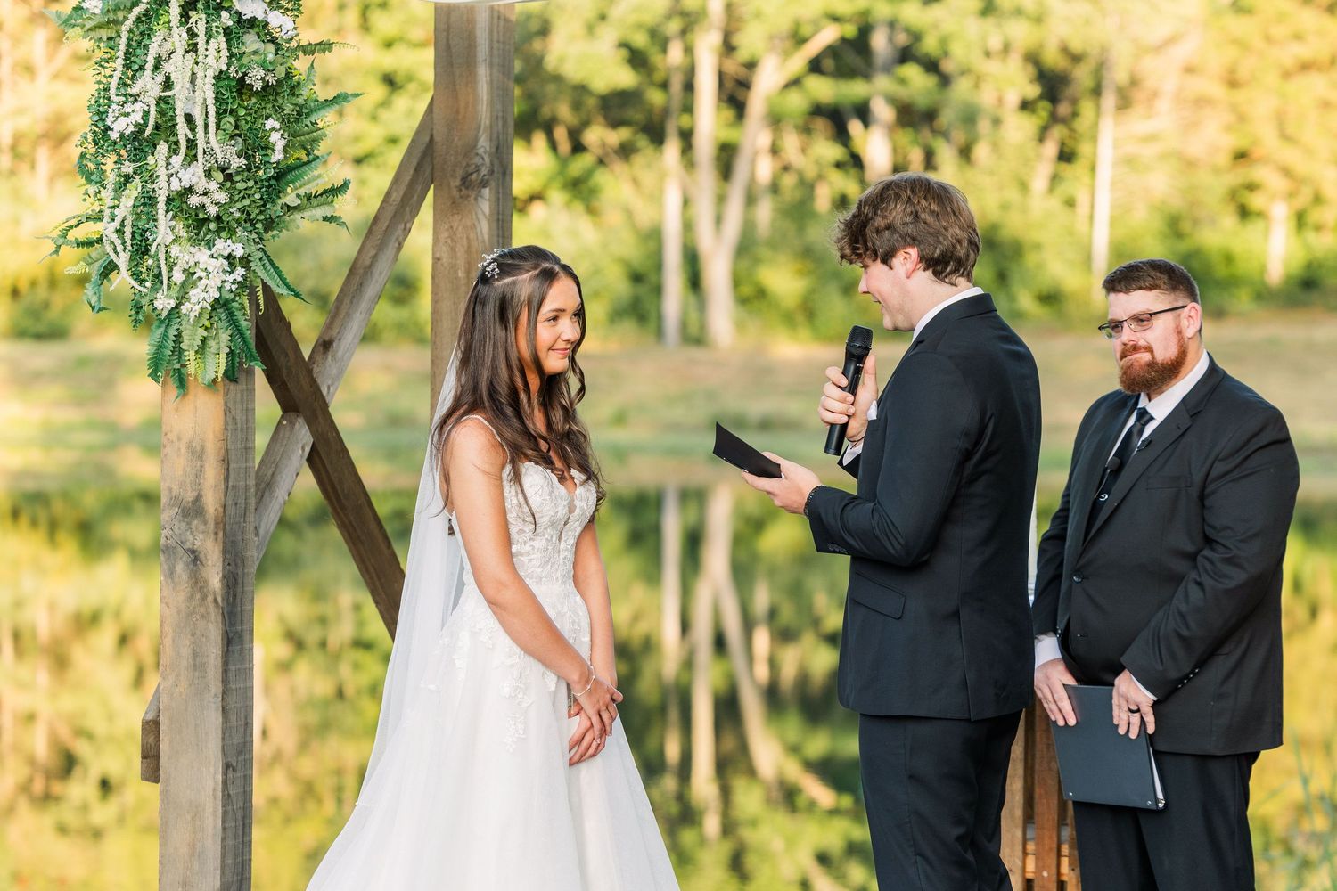 Wedding couple exchanging vows beneath rustic wooden arbor at sunset.